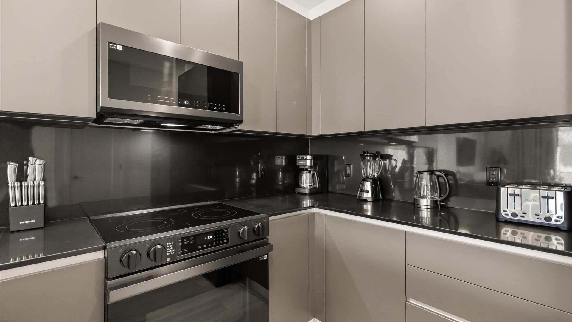 Kitchen countertop area with black backsplash, showcasing small appliances including a coffee maker, blender, toaster, and electric kettle, alongside a knife block.