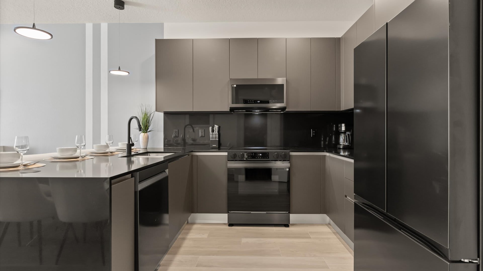 Contemporary kitchen with dark gray flat-panel cabinets, black countertops, and a black backsplash, featuring a stainless steel range, microwave, and a large refrigerator.