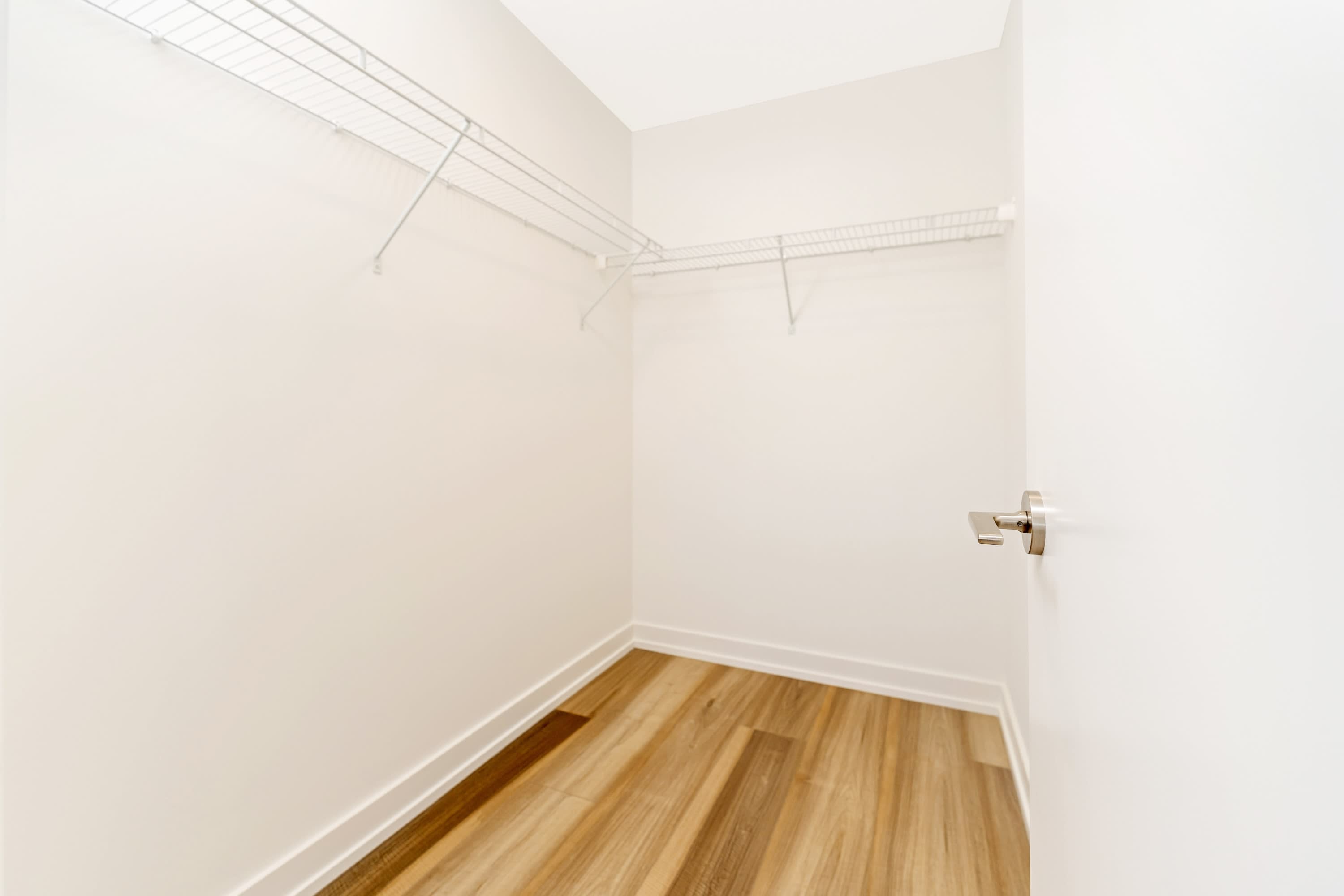 An empty walk-in closet with white wire shelving installed on three walls, featuring light wood-look flooring and clean white walls.