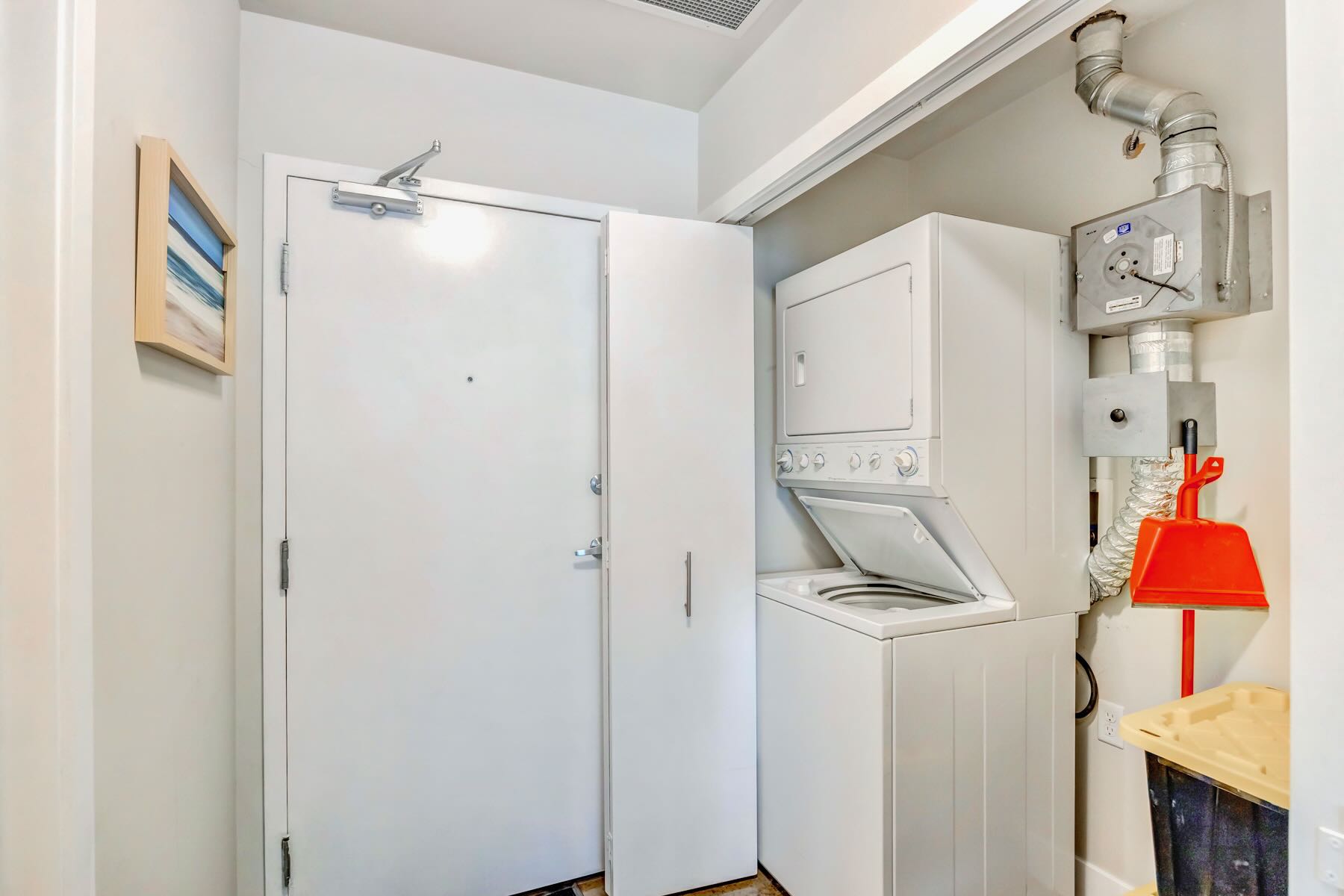 Compact laundry area featuring a stacked white washer and dryer unit, located in a utility closet near the entrance door.