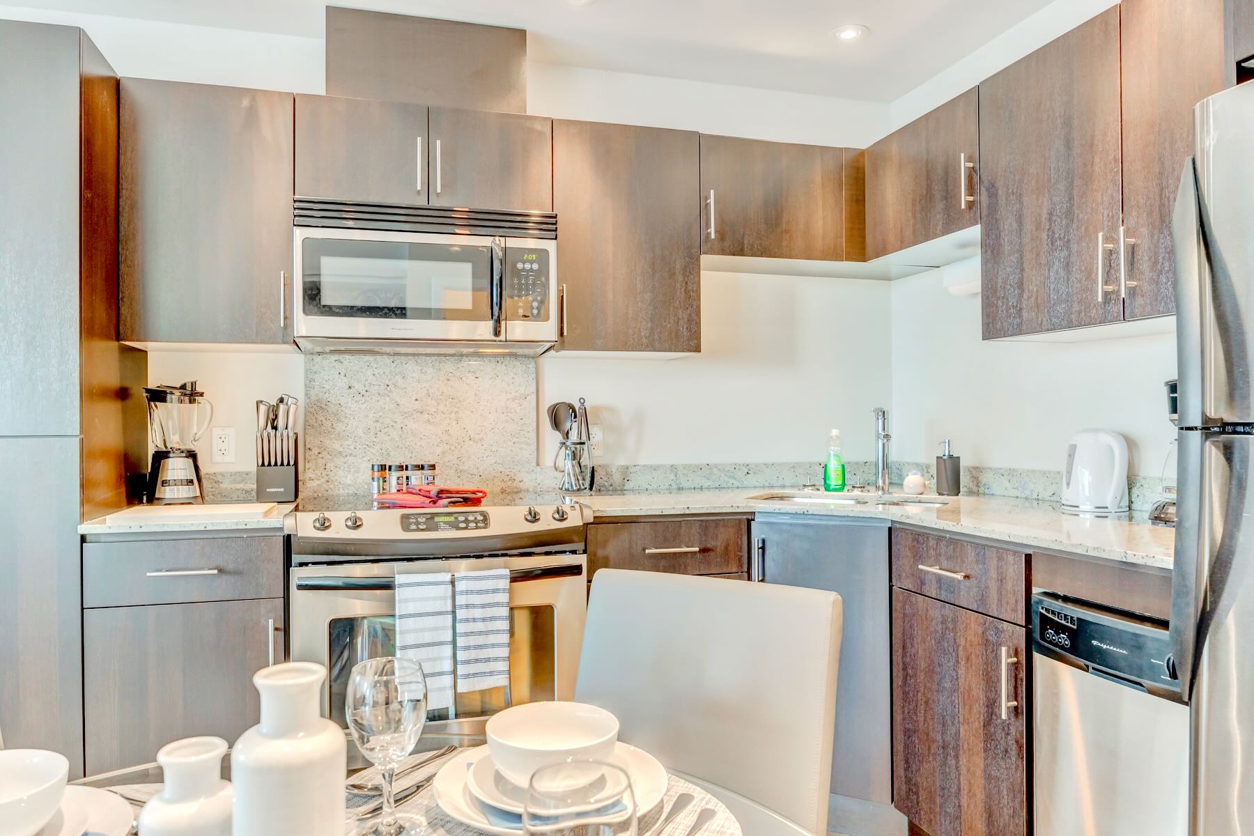 Detailed view of the modern kitchen featuring dark wood cabinets, light granite countertops, a stainless steel microwave above a range, and a double sink with a gooseneck faucet.