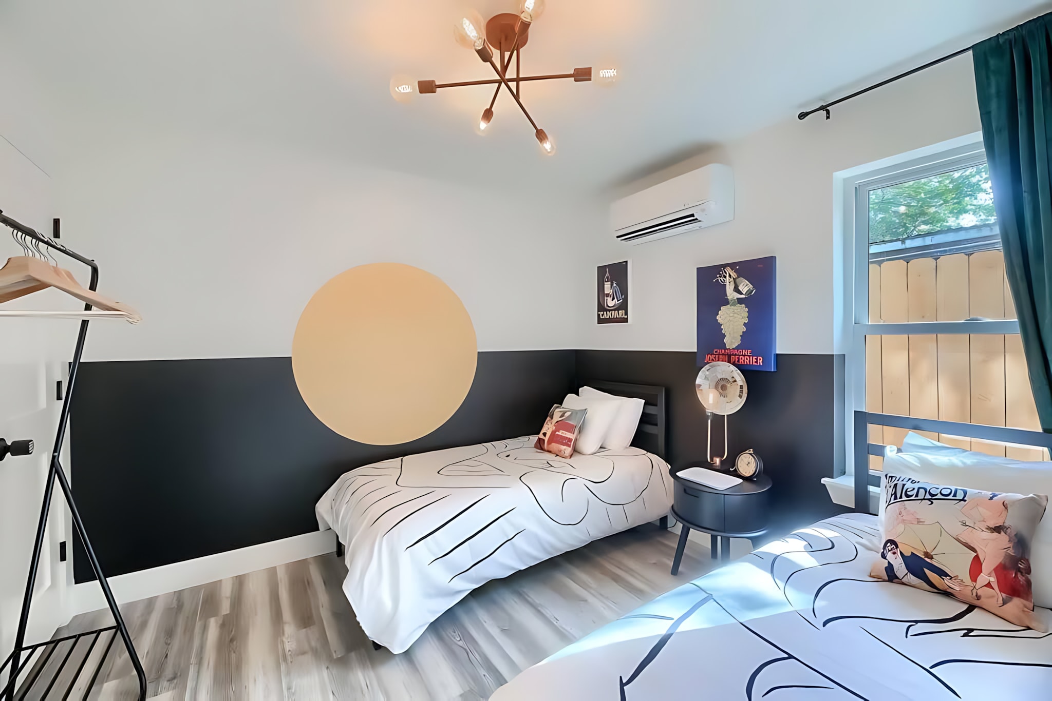 A wider view of the twin bedroom, revealing a large circular decal on the wall above one of the beds, alongside the vintage posters and the modern light fixture.