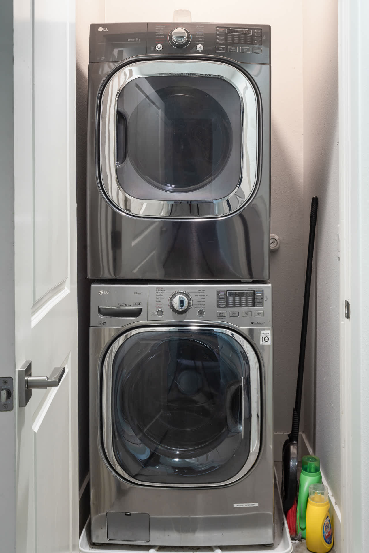 Compact laundry closet featuring a stacked silver LG washer and dryer unit, with cleaning supplies neatly placed beside it.