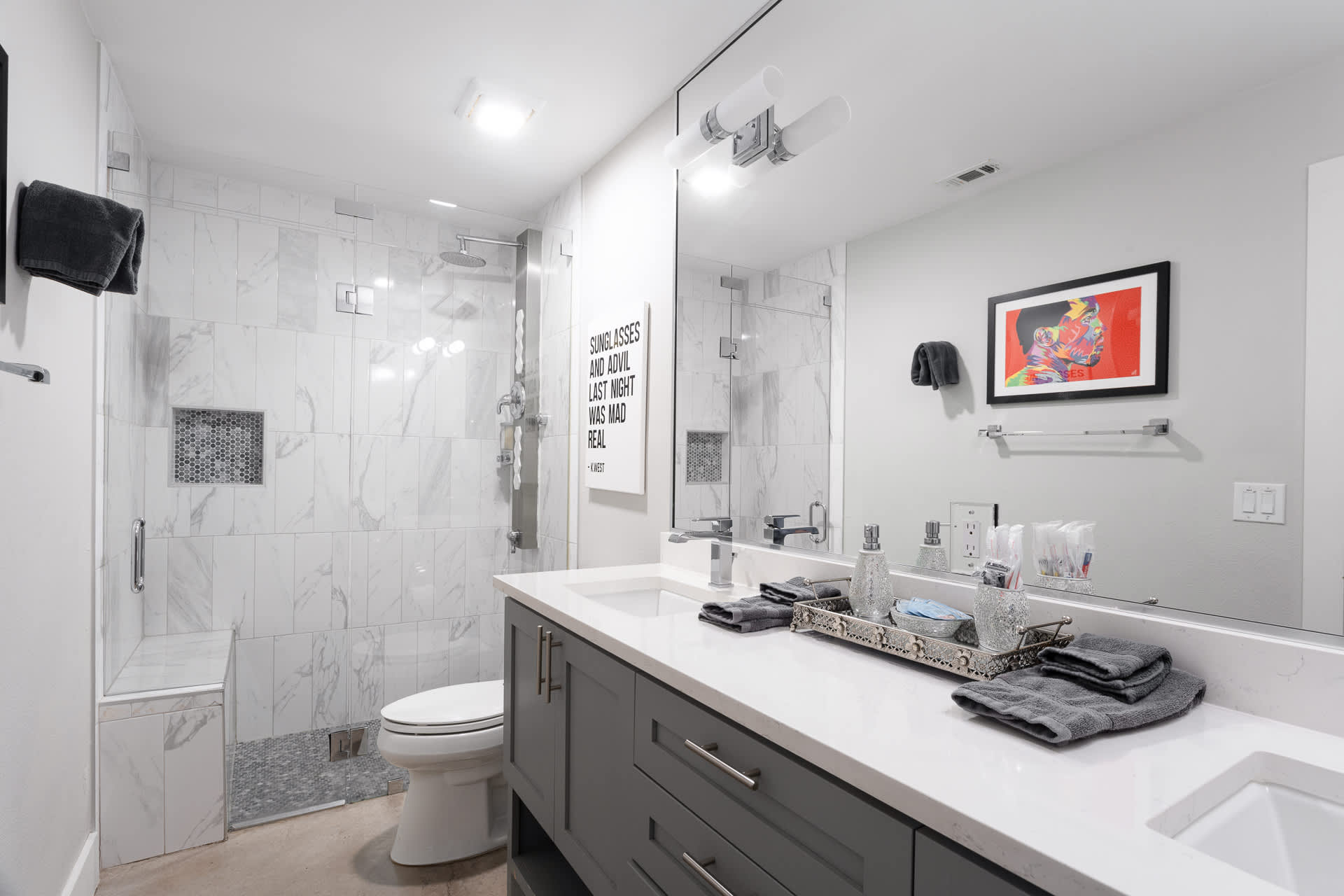 Contemporary bathroom with a large walk-in shower featuring white marble-look tiles and a built-in bench, alongside a toilet and a double vanity with a large mirror.