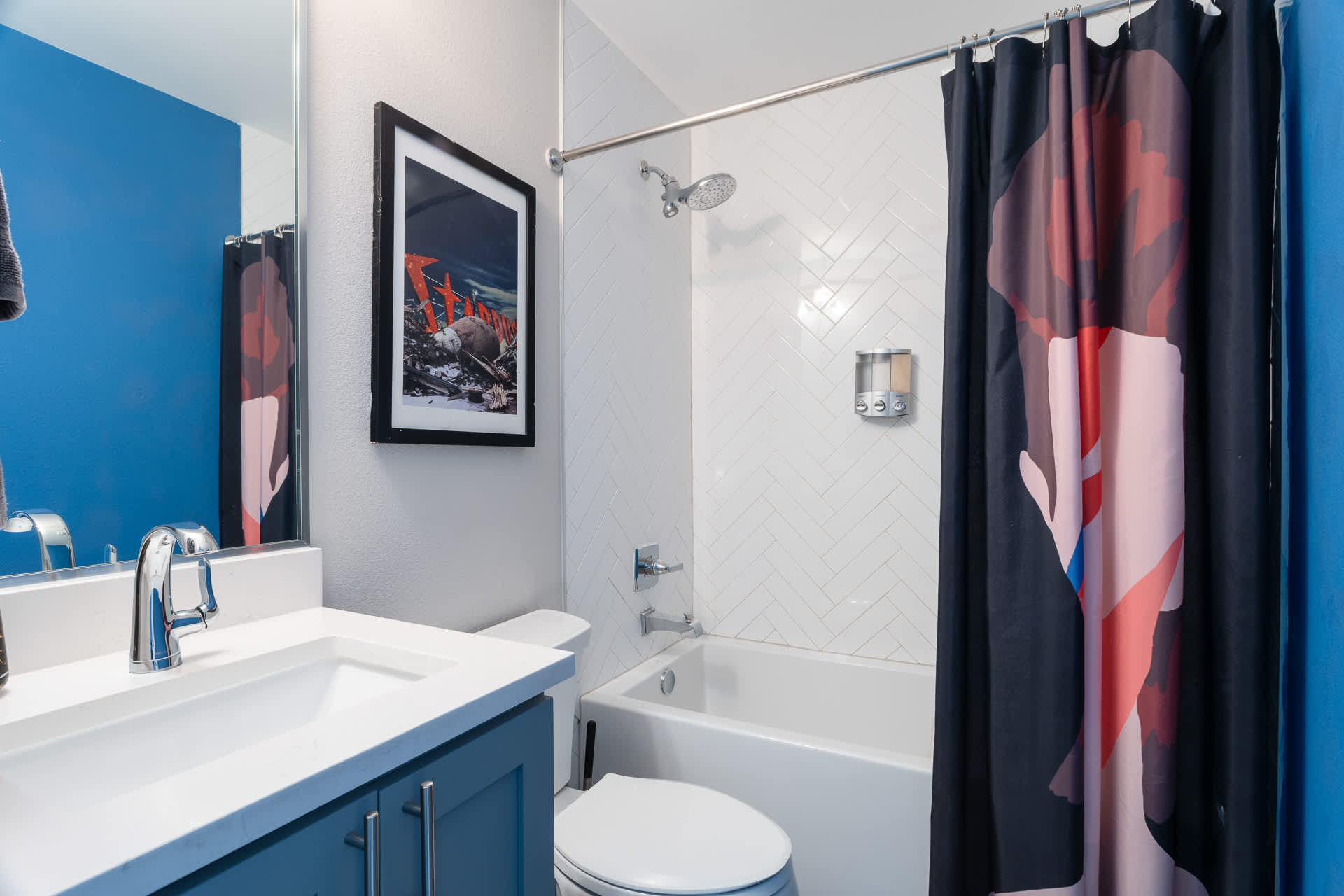 Modern bathroom with a white subway tile shower/tub combo, a dark blue accent wall, and a white vanity with a single sink and chrome faucet, featuring a colorful shower curtain.