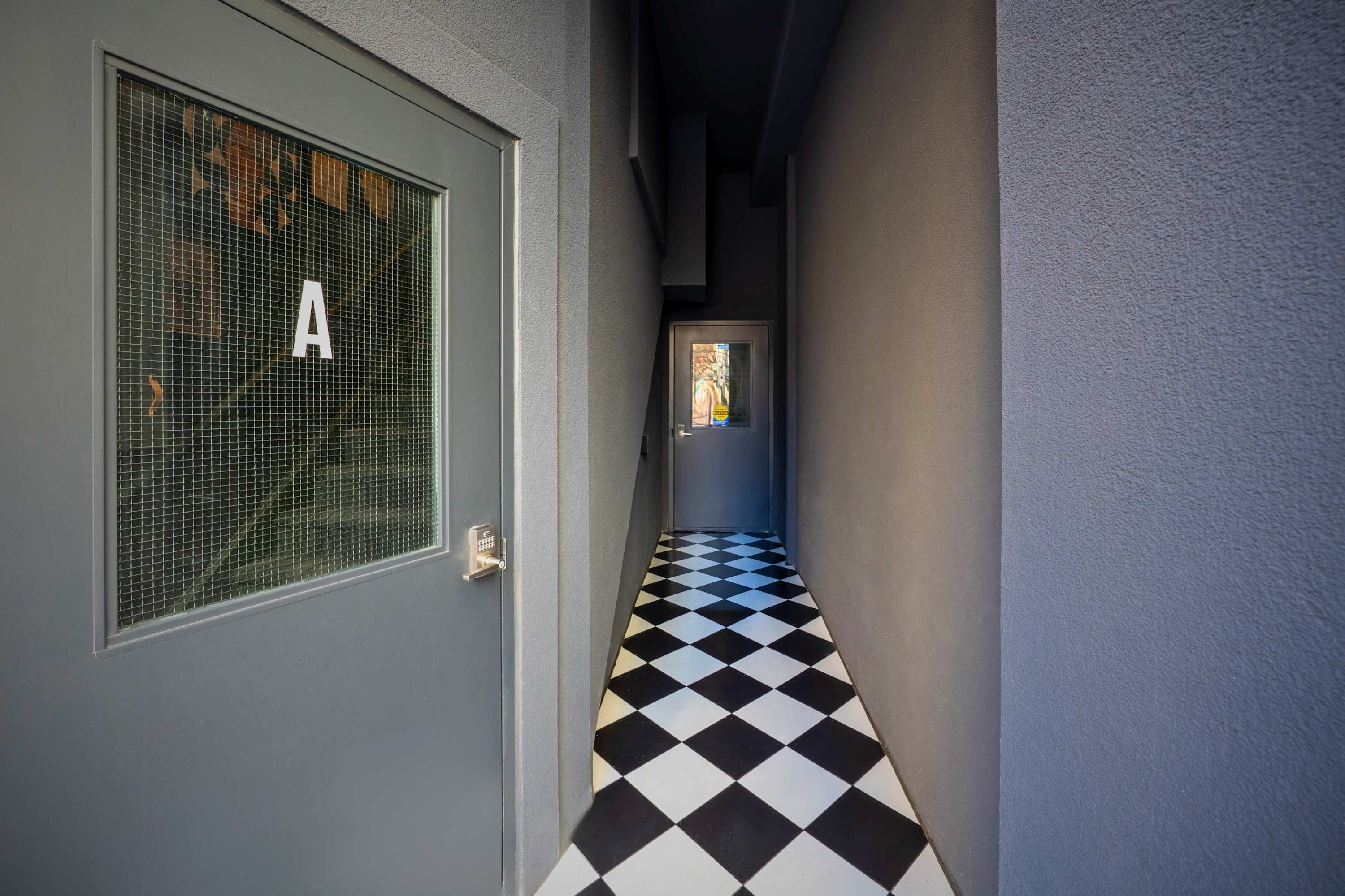 A narrow interior hallway with a striking black and white checkered floor, leading towards a door at the end, with a grey door labeled "A" on the left.
