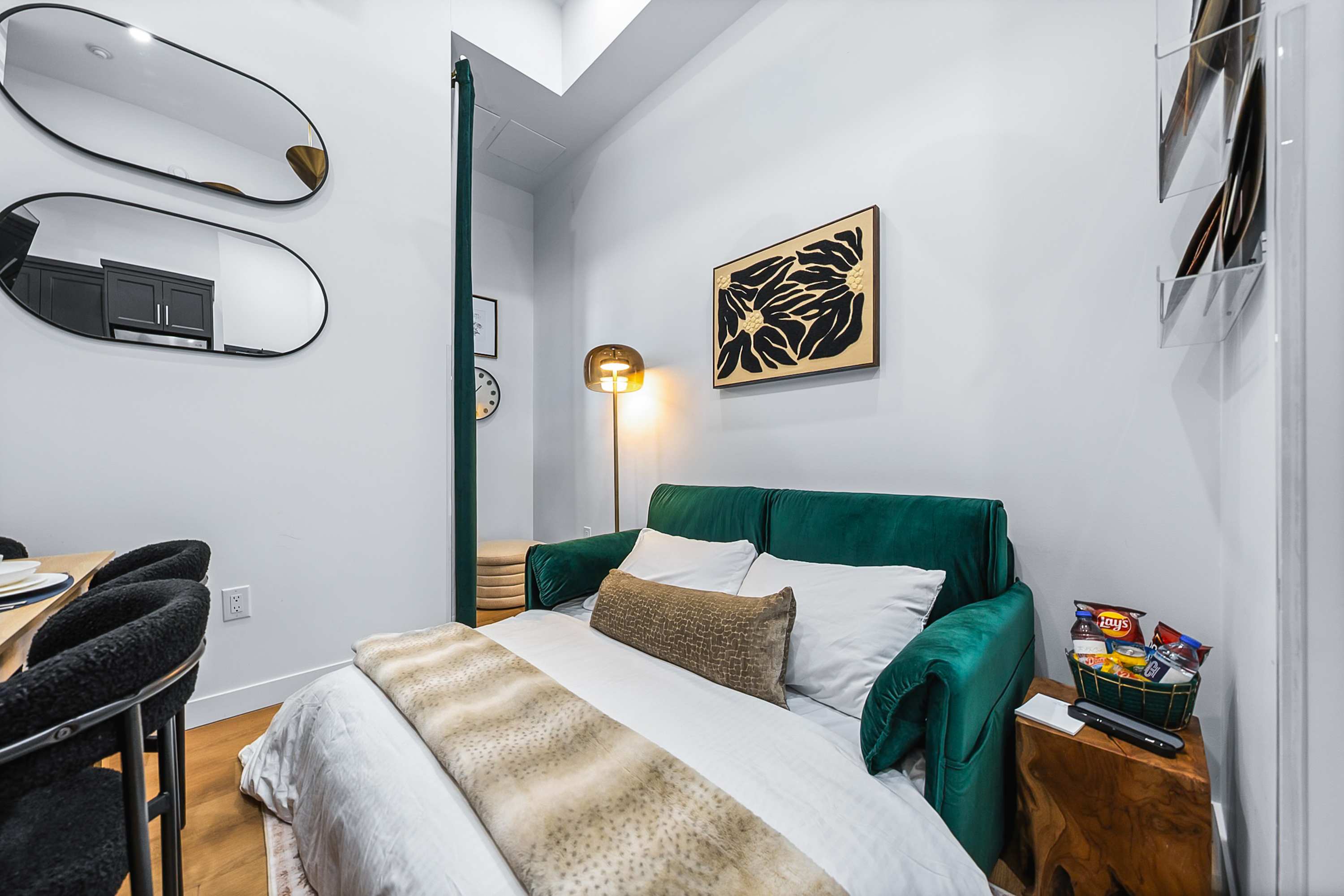 The emerald green sofa transformed into a comfortable pull-out bed, dressed with white linens and a faux fur throw, indicating a flexible sleeping arrangement in the living area.