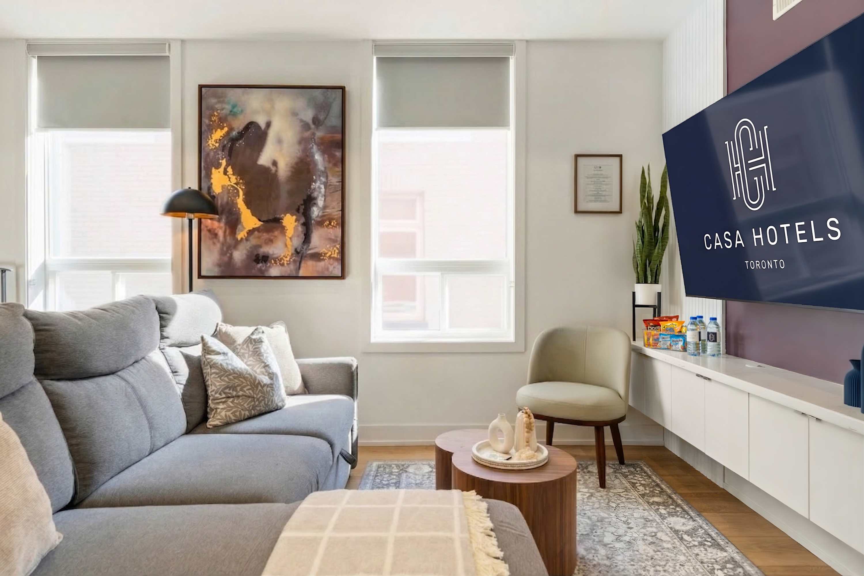 Inviting living room with a grey sectional sofa, a pair of round wooden coffee tables, and a cream accent chair. A large flat-screen TV is mounted on a deep purple accent wall, above a white floating media console.