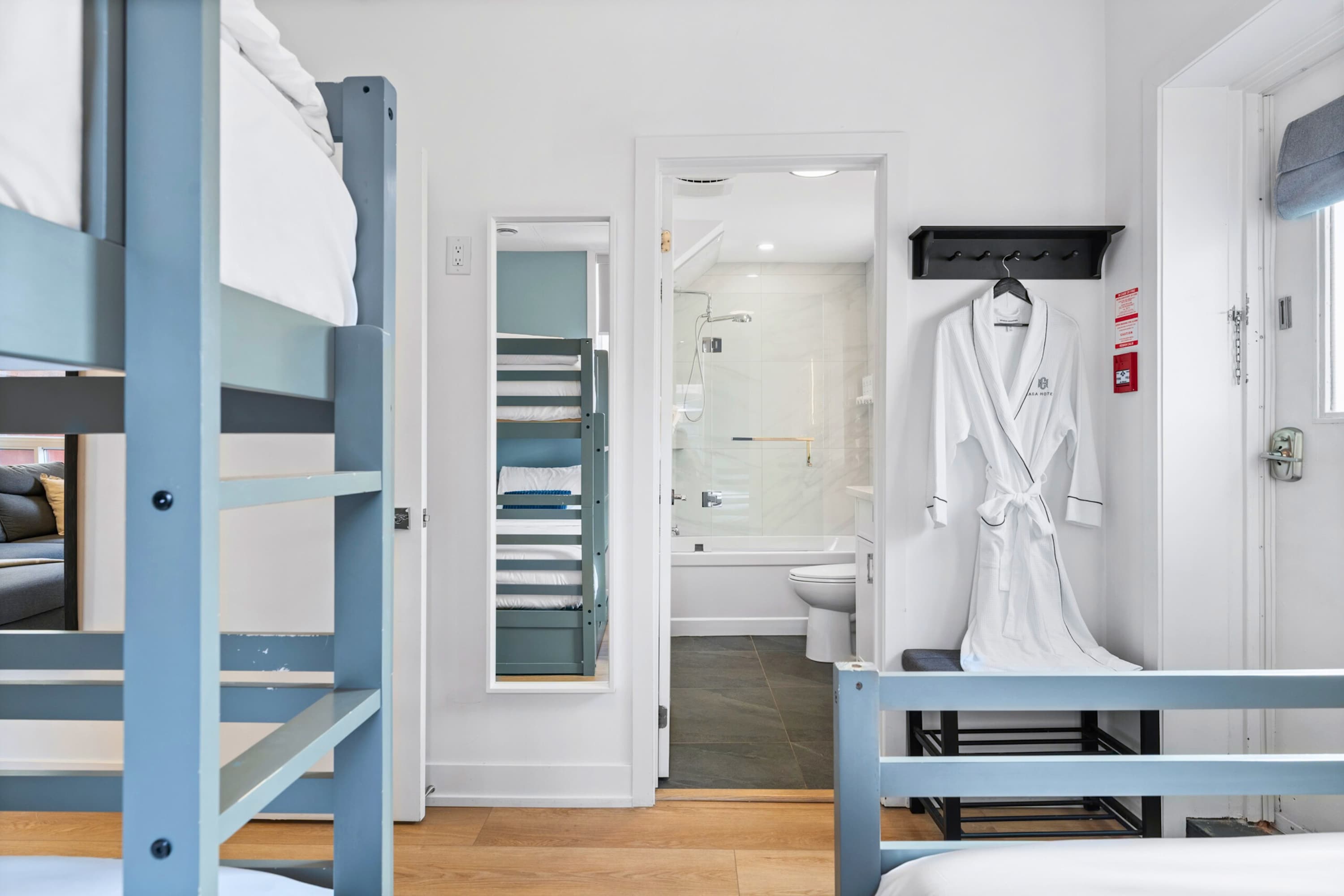 View from the bunk bed room looking into a bathroom with a bathtub and toilet, showing a full-length mirror and a white bathrobe hanging on a hook.