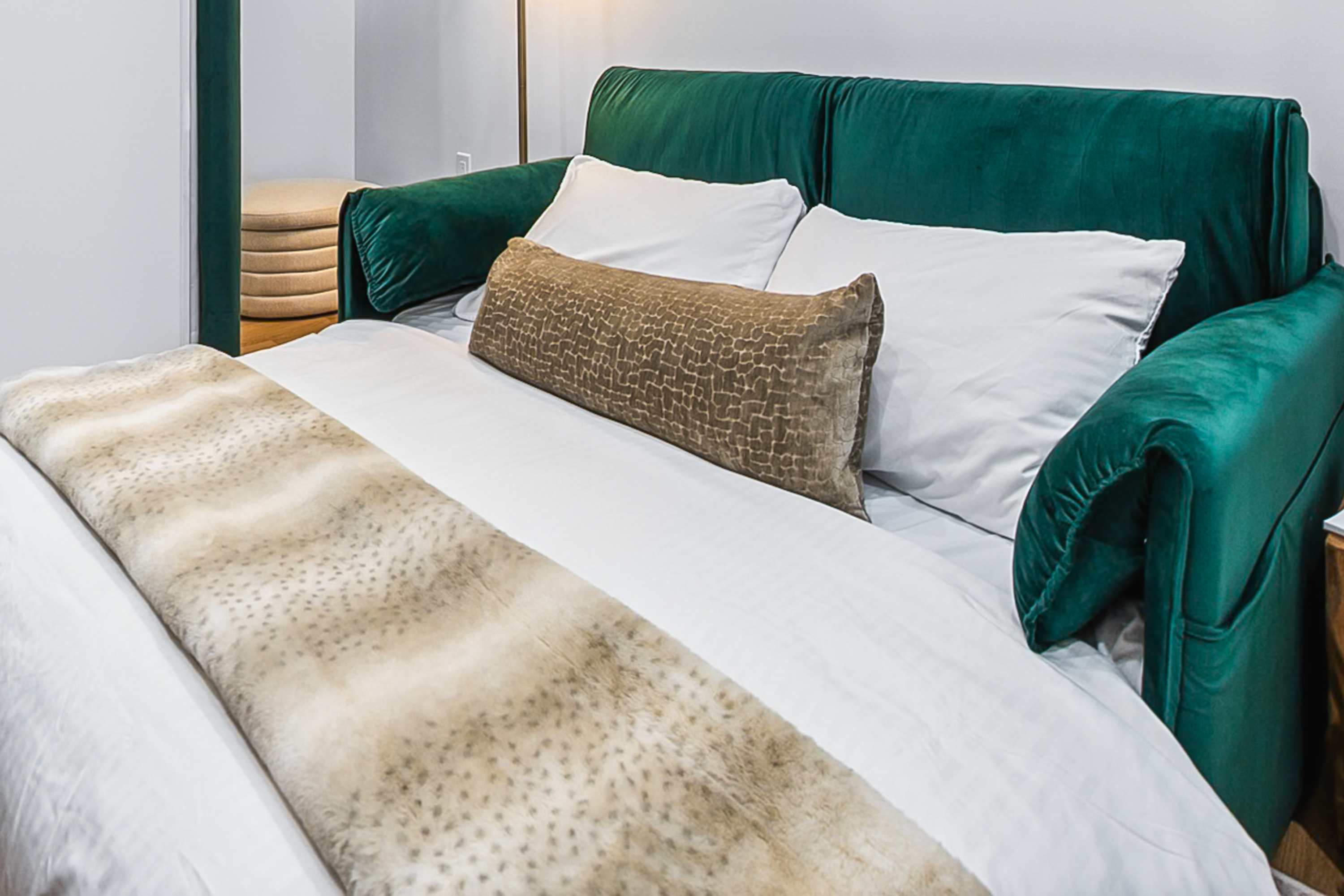 Close-up of a green velvet sofa bed with white pillows and a textured brown and beige throw blanket. The sofa arms are plush and rounded.