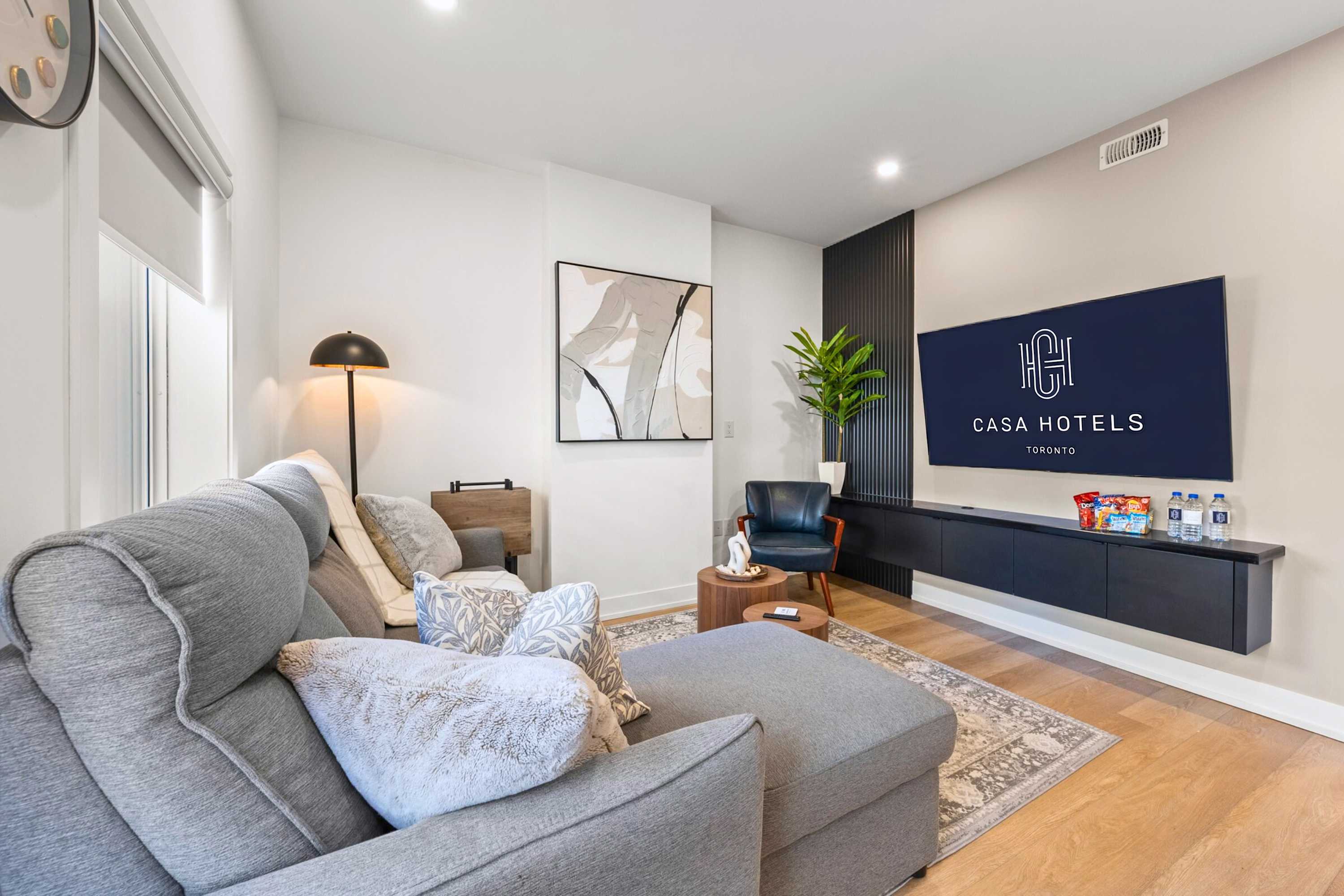 View of the living room from a different angle, showcasing the gray sectional sofa with decorative pillows, a floor lamp, and the wall-mounted TV area with a dark slatted accent wall.
