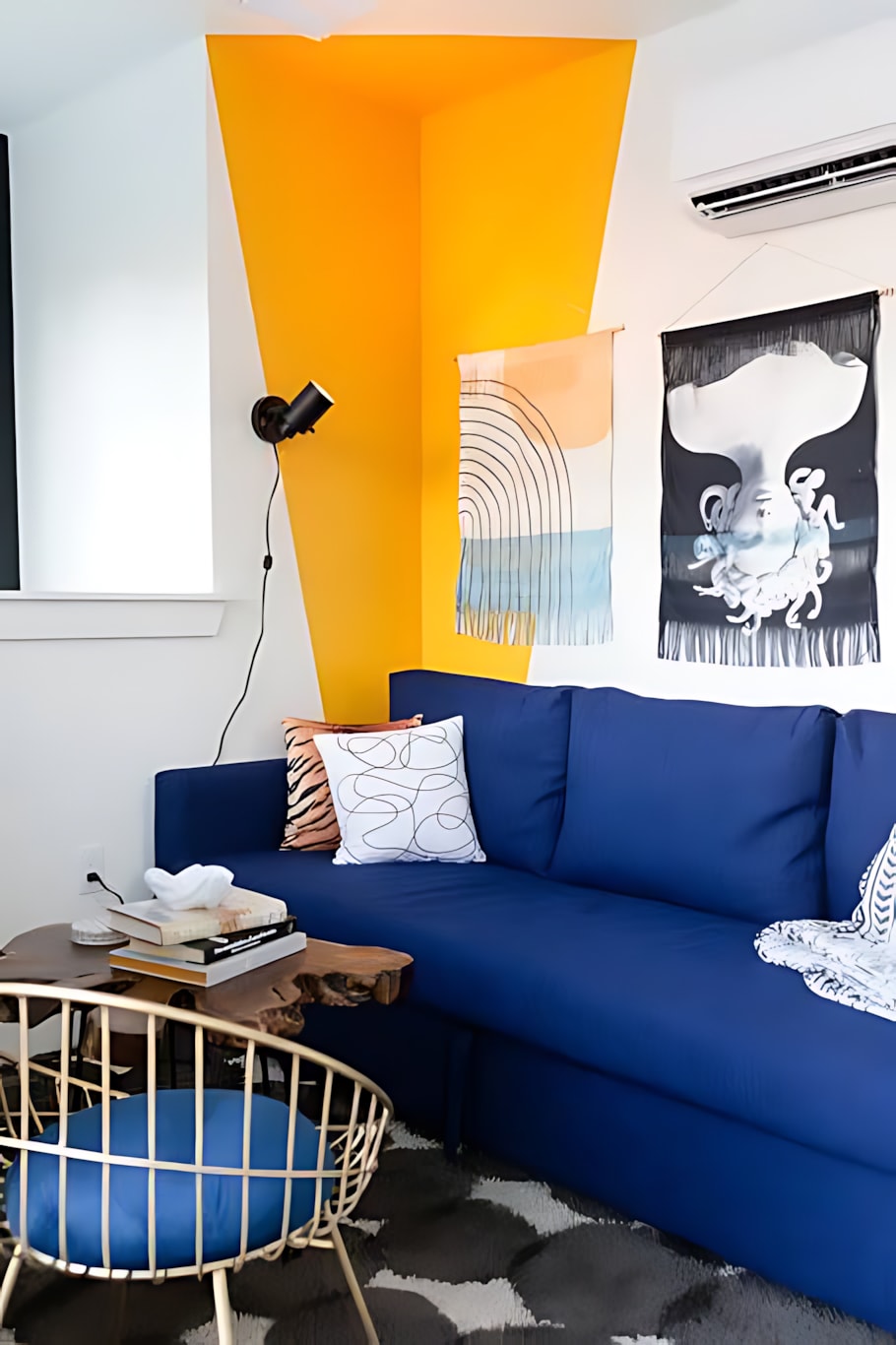 A vibrant living space featuring a royal blue sofa against a white wall with a bold orange geometric accent, complemented by modern wall art and a small wooden side table.