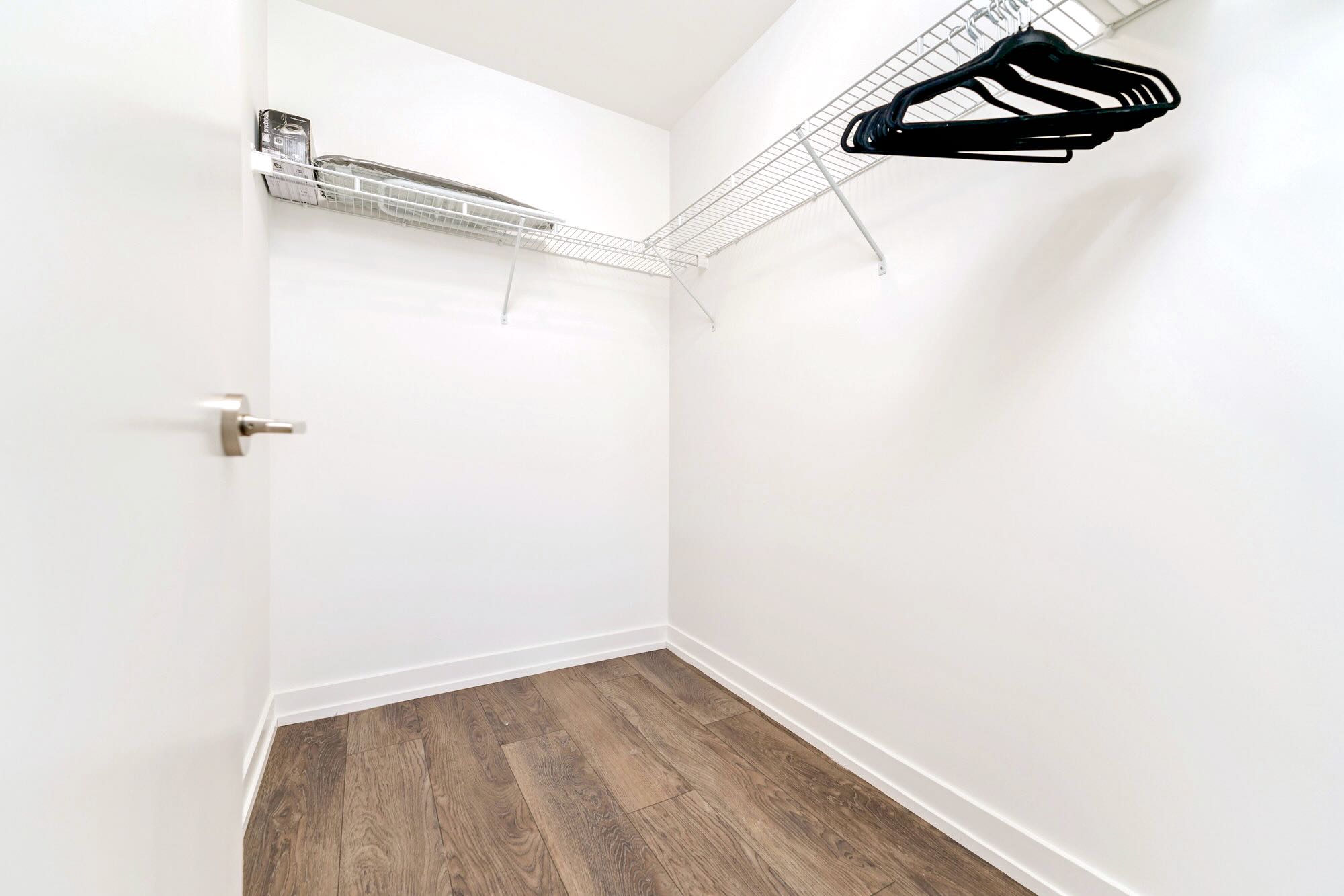 Empty walk-in closet with white walls, light wood-look flooring, and wire shelving with hangers, providing ample storage space.