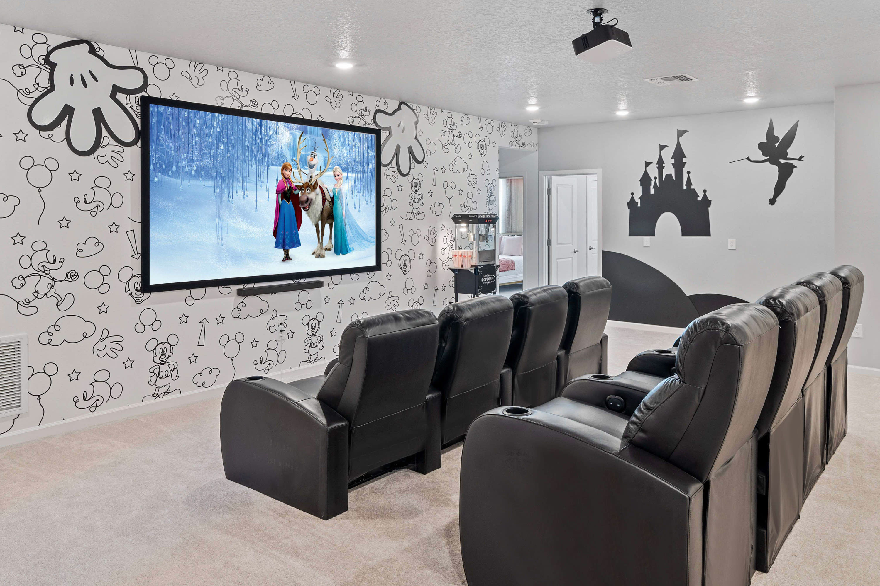 Cozy media room with a large projection screen displaying "Frozen," surrounded by black and white Disney-themed wall art, and multiple rows of black reclining theater seats.