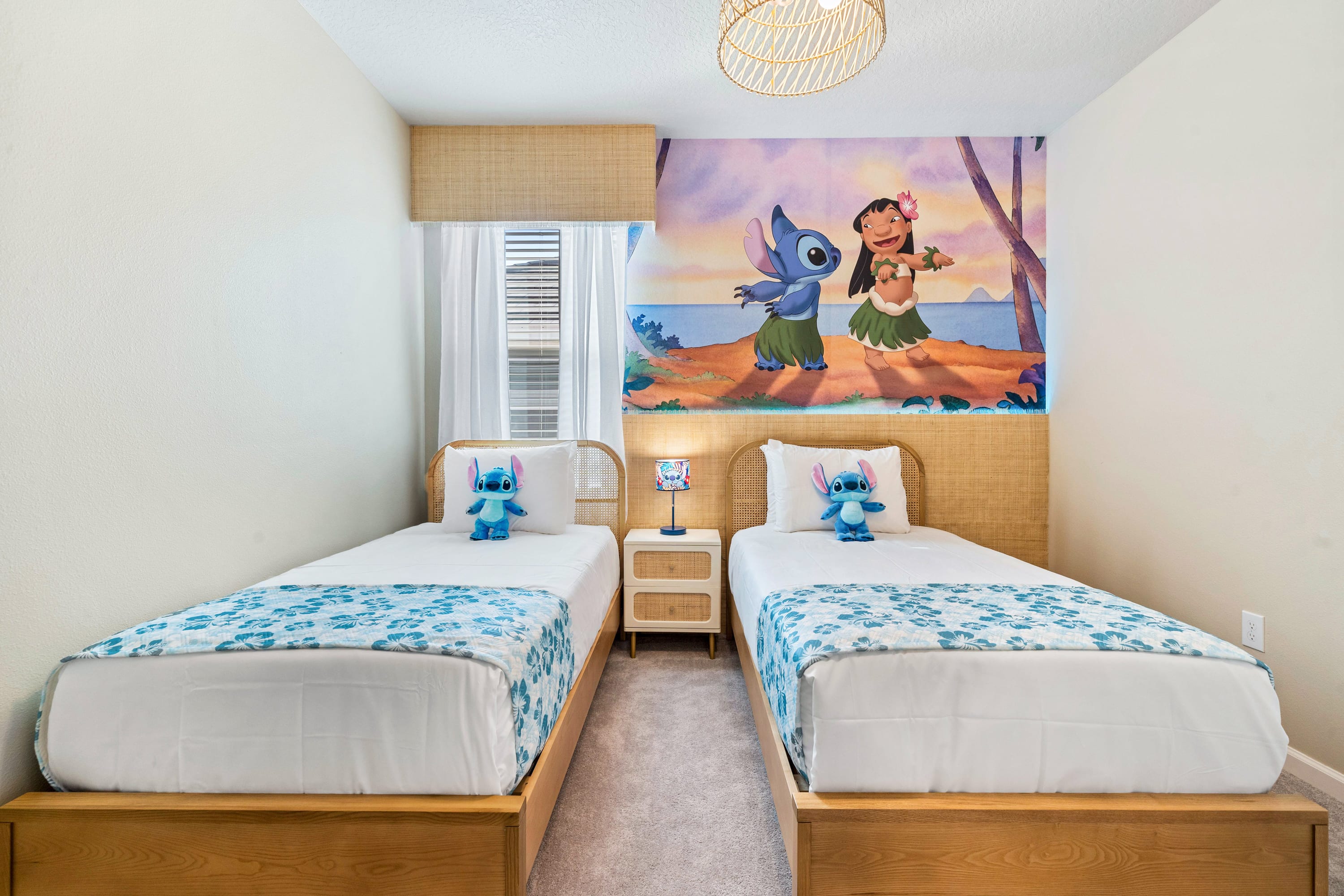 A vibrant Lilo & Stitch themed children's bedroom with two twin beds featuring natural wood frames and woven headboards. A colorful mural of Lilo and Stitch on a beach covers the wall above the beds, and each bed has a Stitch plush toy.