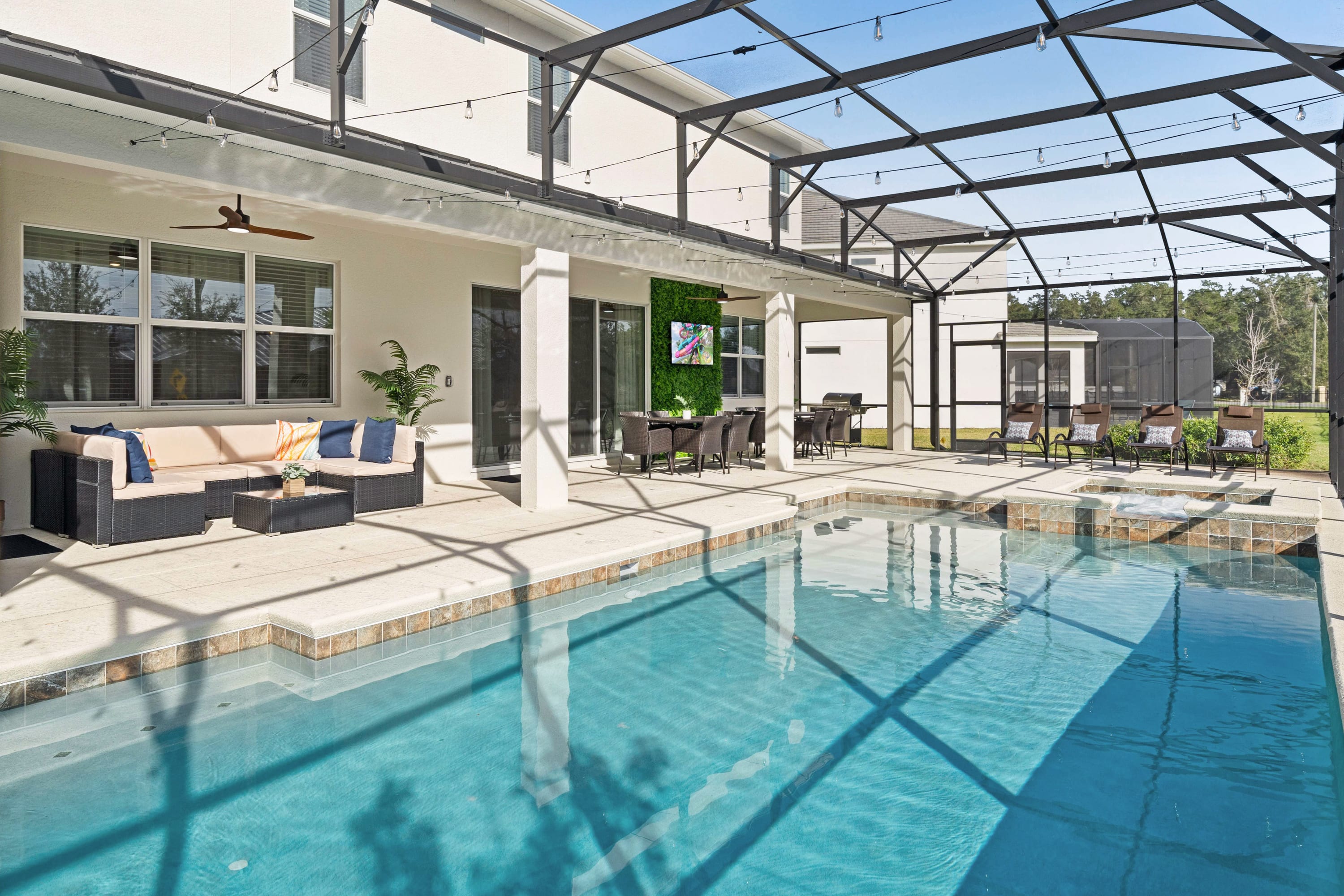 Expansive screened pool area featuring a large swimming pool, an outdoor lounge area with a sectional sofa, and an outdoor dining set, all under a covered patio.