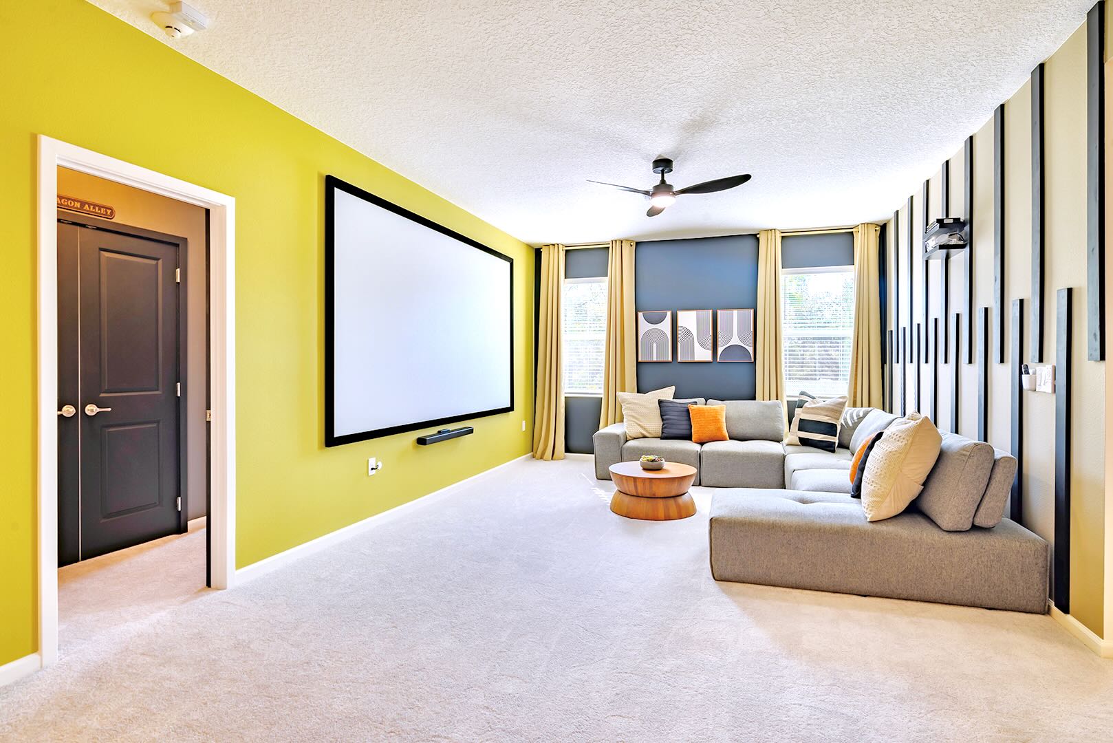 Spacious media room with a large projection screen on a lime green accent wall, a comfortable grey sectional sofa with throw pillows, and a modern wooden coffee table, perfect for entertainment.
