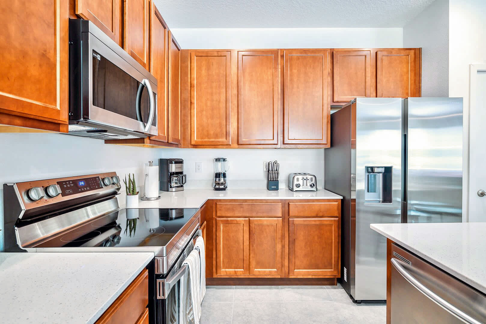 Well-equipped kitchen with light wood cabinetry, white quartz countertops, and stainless steel appliances including a microwave, electric range, and side-by-side refrigerator, complemented by a coffee maker and toaster.