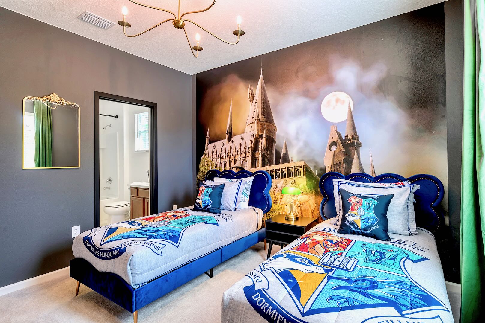 Enchanting themed bedroom with two blue velvet twin beds, a striking Hogwarts castle mural, and a modern gold chandelier, offering a whimsical and comfortable space for young guests.