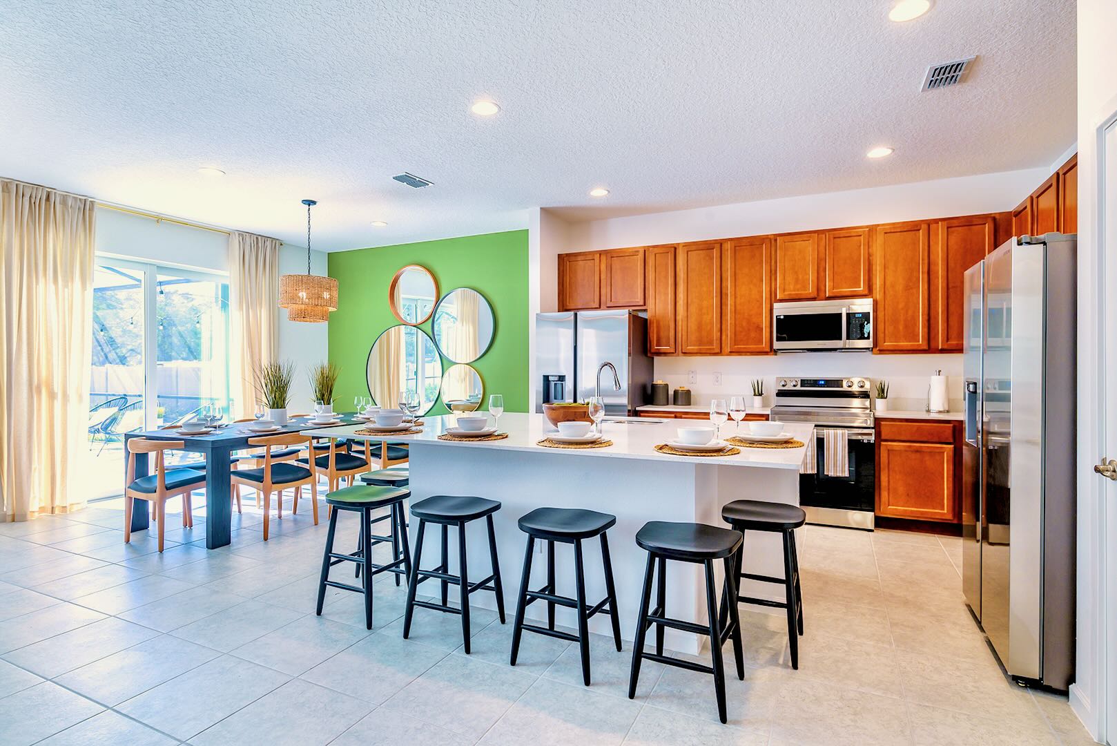 Modern open-concept kitchen and dining area featuring a white quartz island with four black bar stools, light wood cabinetry, and a dining table with blue chairs, all set against a vibrant lime green accent wall.