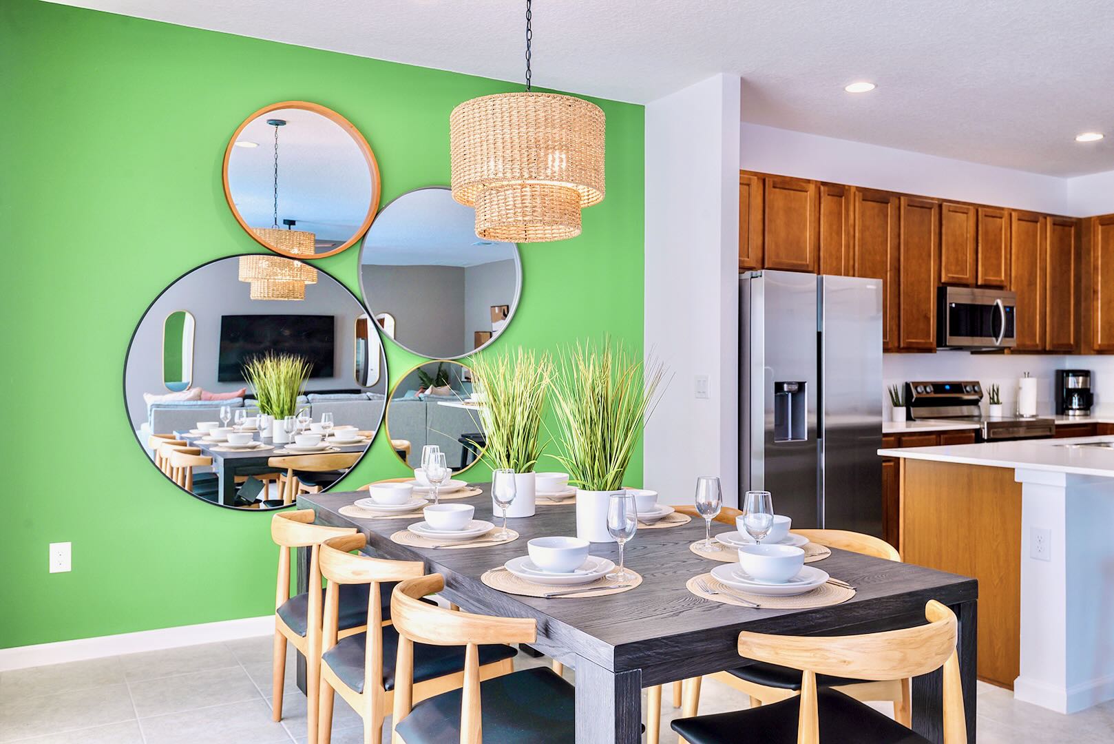Vibrant dining area with a lime green accent wall adorned with circular mirrors, featuring a dark rectangular dining table set for eight with modern wooden chairs, and a woven pendant light fixture.