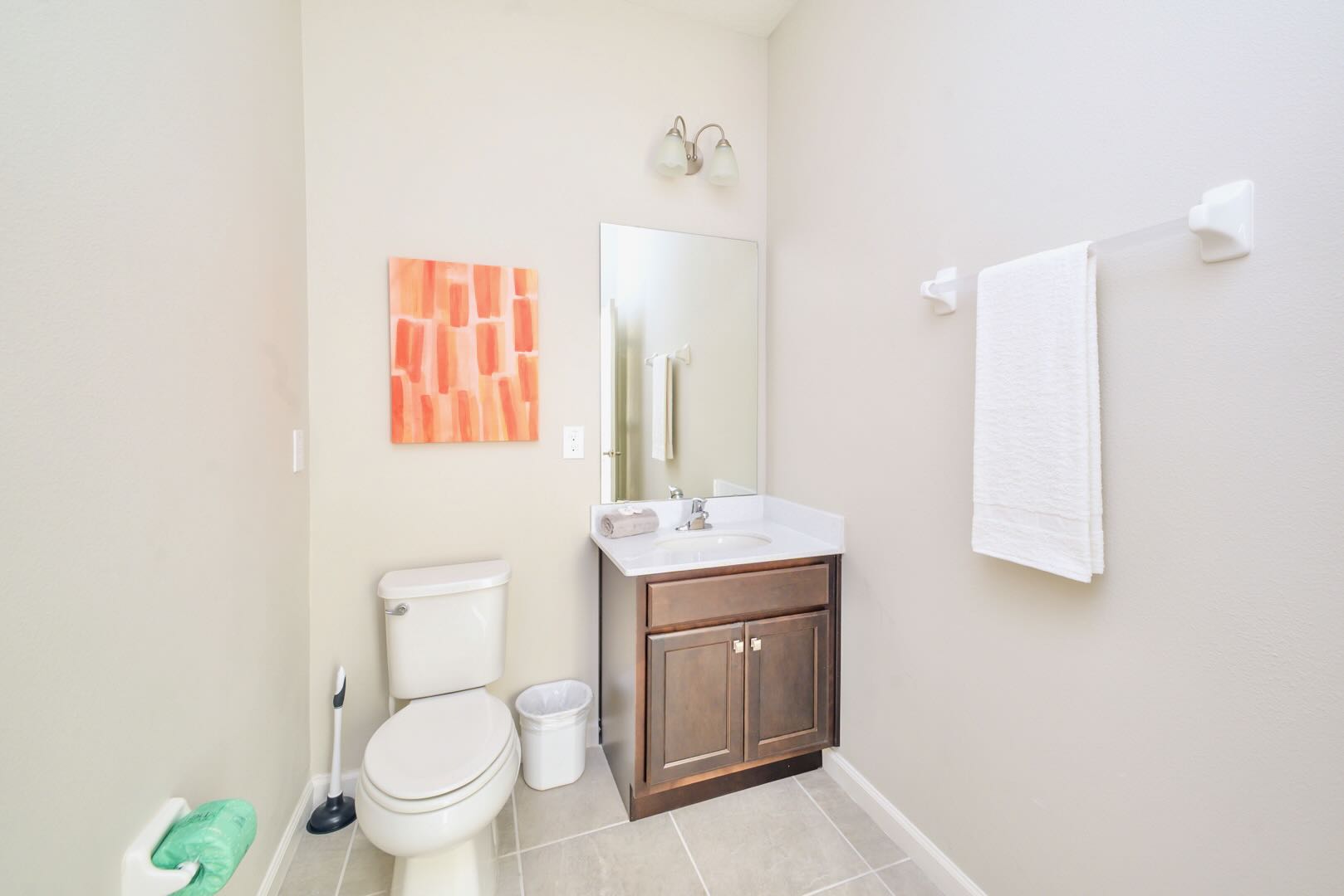 Small bathroom with a single dark wood vanity, white sink, and a toilet. A mirror hangs above the vanity, and a colorful abstract painting adorns the wall.
