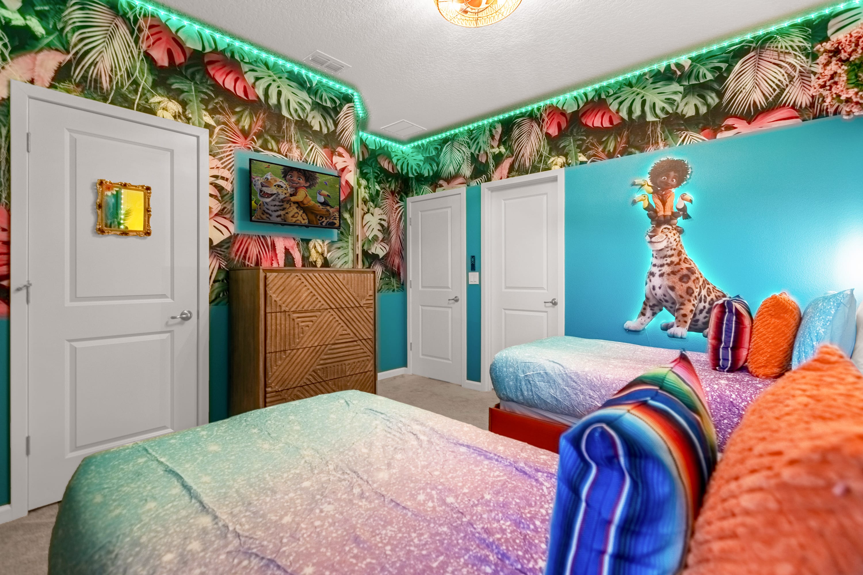 Colorful themed bedroom with two twin beds, one visible in the foreground, featuring vibrant bedding and a wall mural depicting a jungle scene with characters, illuminated by green LED strip lighting.