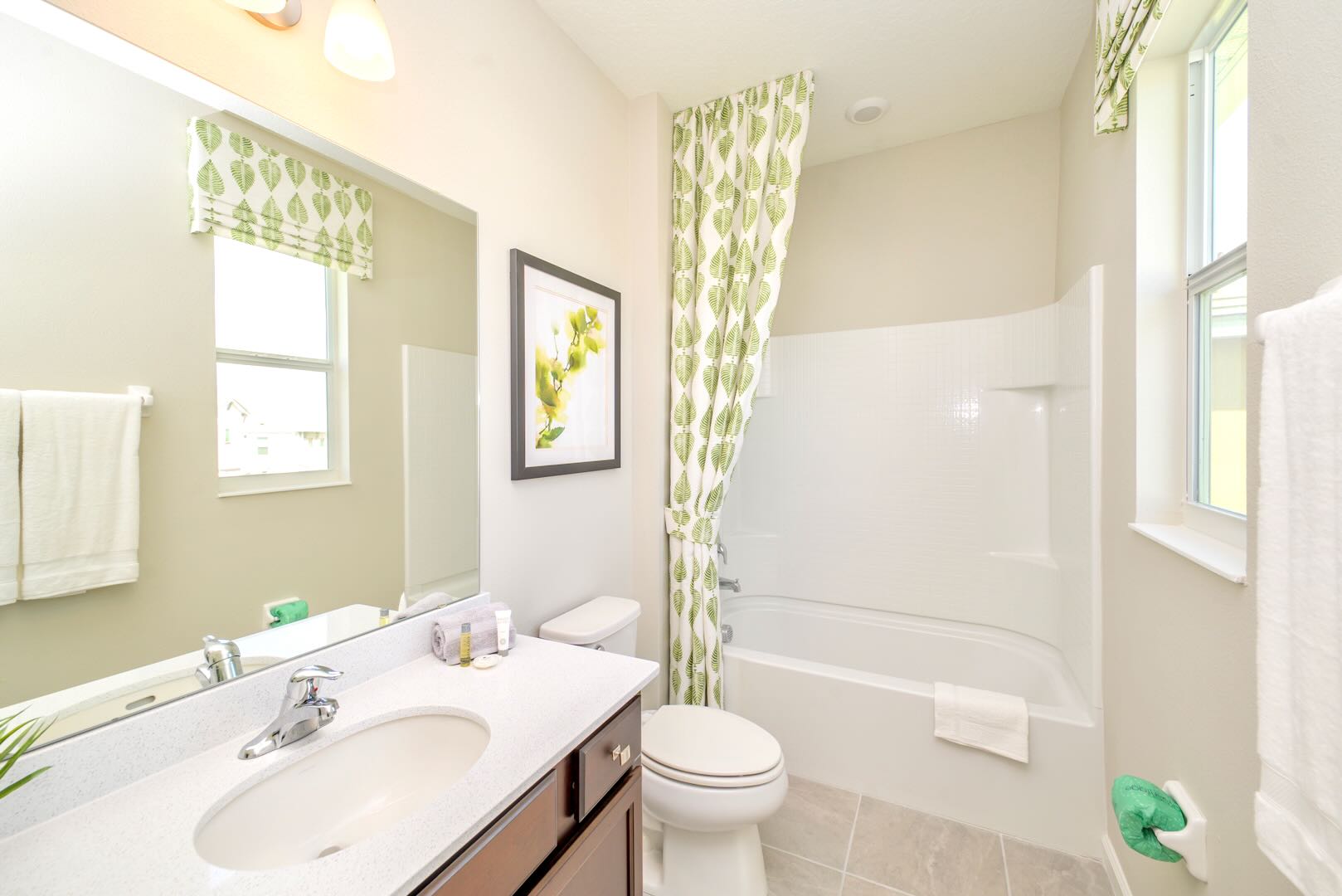 Bright bathroom with a white vanity, single sink, dark wood cabinet, and a shower/tub combo with a vibrant green leaf-patterned shower curtain and matching window valance.