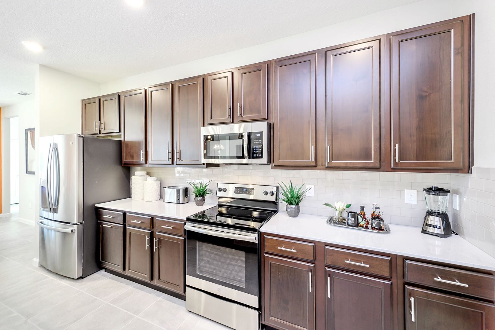 Detailed view of the kitchen counter with white subway tile backsplash, dark wood cabinetry, and stainless steel appliances including a range with an oven and an over-the-range microwave. Small decorative plants and kitchen gadgets are neatly arranged.