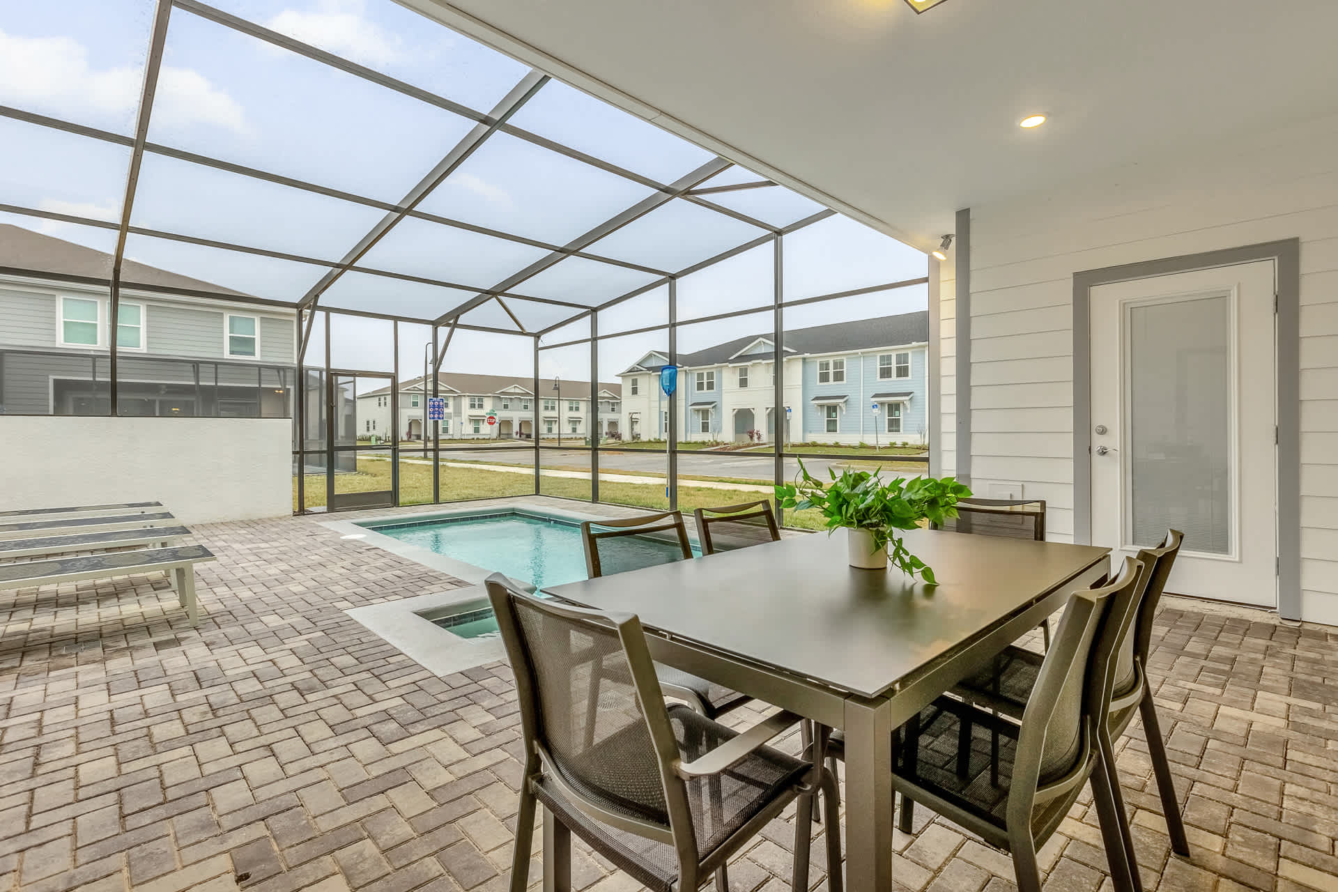 A screened-in patio features an outdoor dining table with six chairs on a paved surface, overlooking a small private pool. The area is covered by a screen enclosure, and the exterior of the house with white siding is visible.