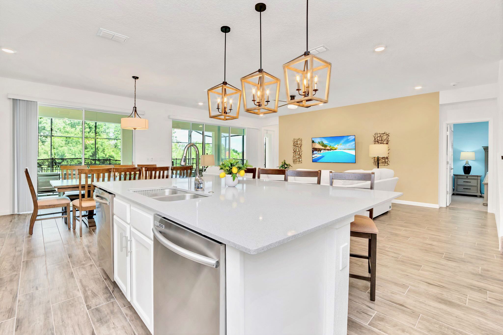 A spacious kitchen island with a white quartz countertop and integrated sink, offering a view of the dining area, living room, and outdoor pool through large glass doors.