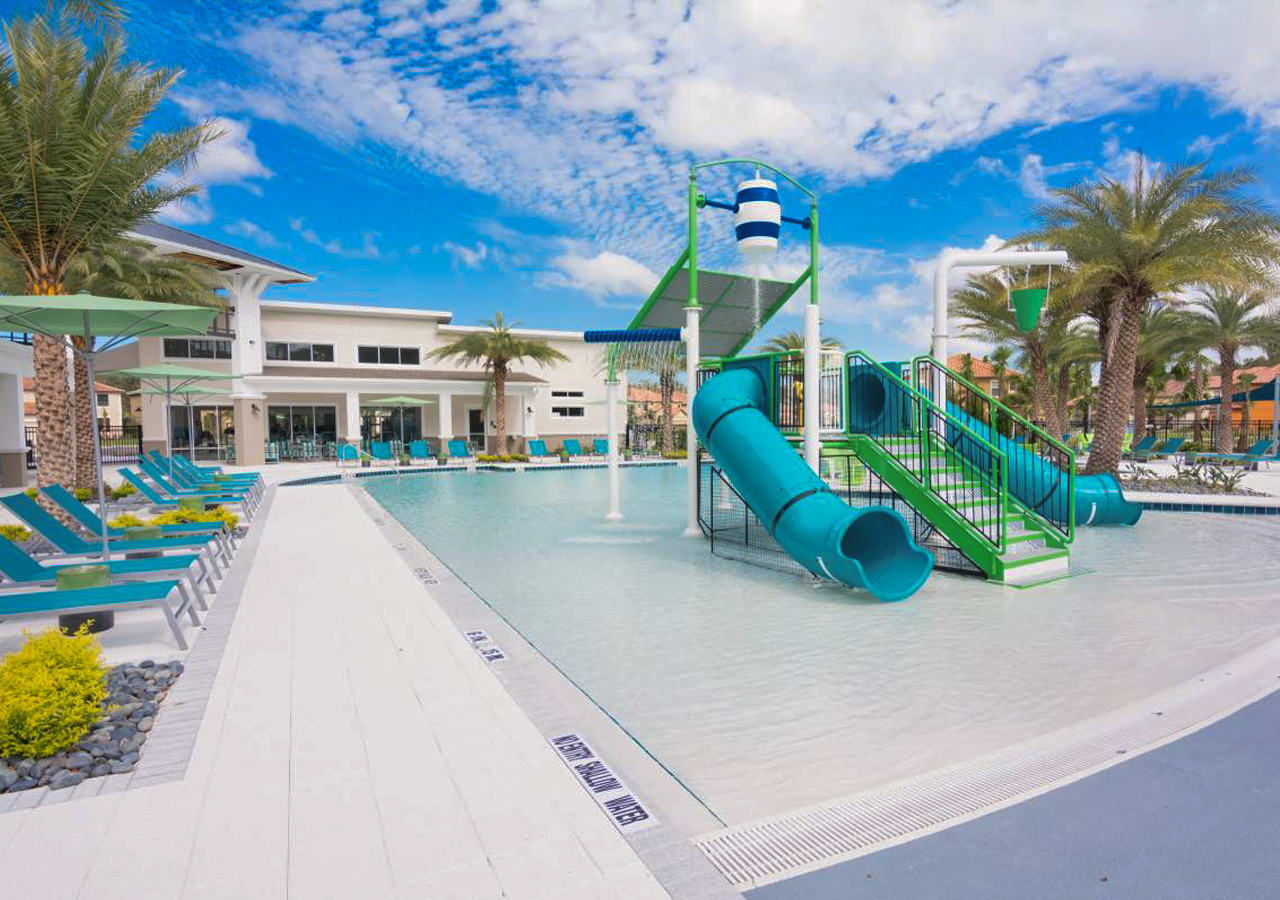 Another view of the resort's children's water play area, showcasing multiple slides and interactive water features in a shallow pool. The surrounding deck is furnished with colorful lounge chairs and umbrellas.