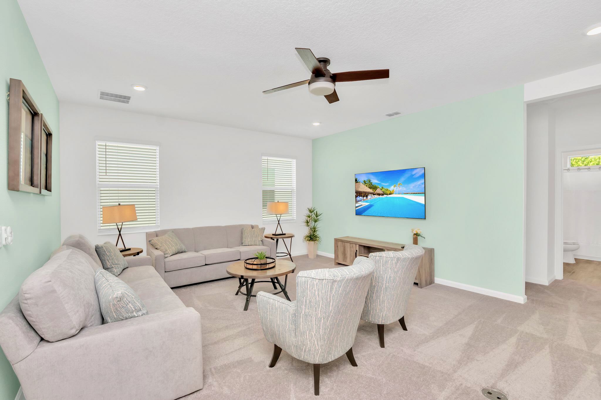 A comfortable upstairs living room with light gray carpet, two sofas, two armchairs, a coffee table, and a wall-mounted TV, featuring a light green accent wall.