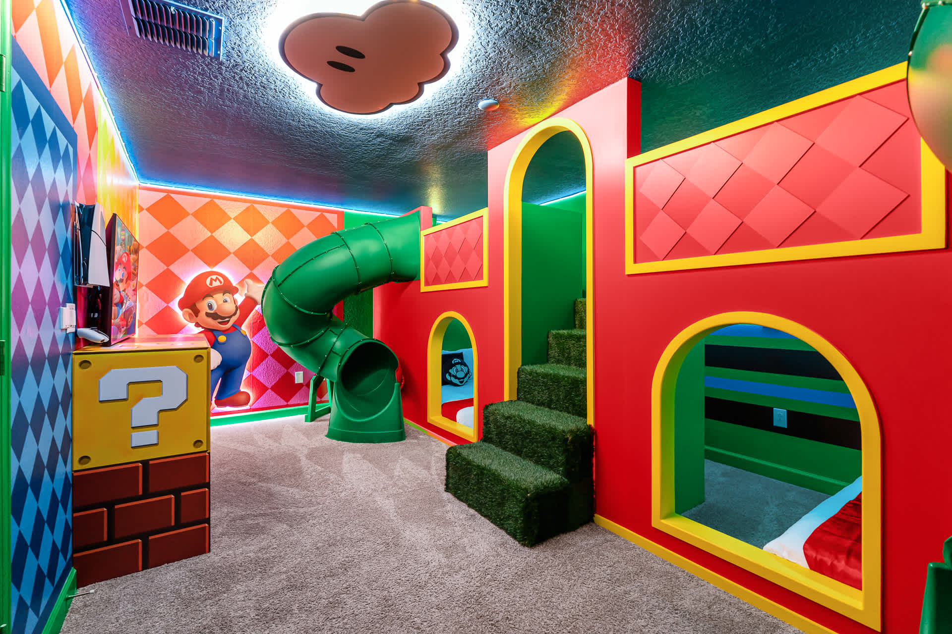 Another view of the "Super Mario" themed room, showcasing the red and green bunk bed structure with arched openings, a green slide, and a large Mario character cutout on the wall.