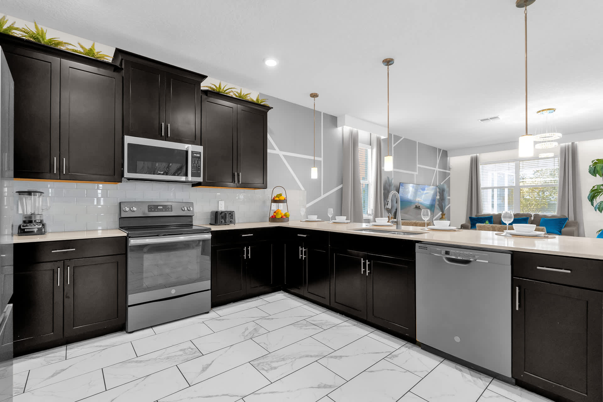 A modern kitchen with dark wood cabinetry, light countertops, and stainless steel appliances including a range, microwave, and dishwasher. A white subway tile backsplash and white tiled floor complete the look.