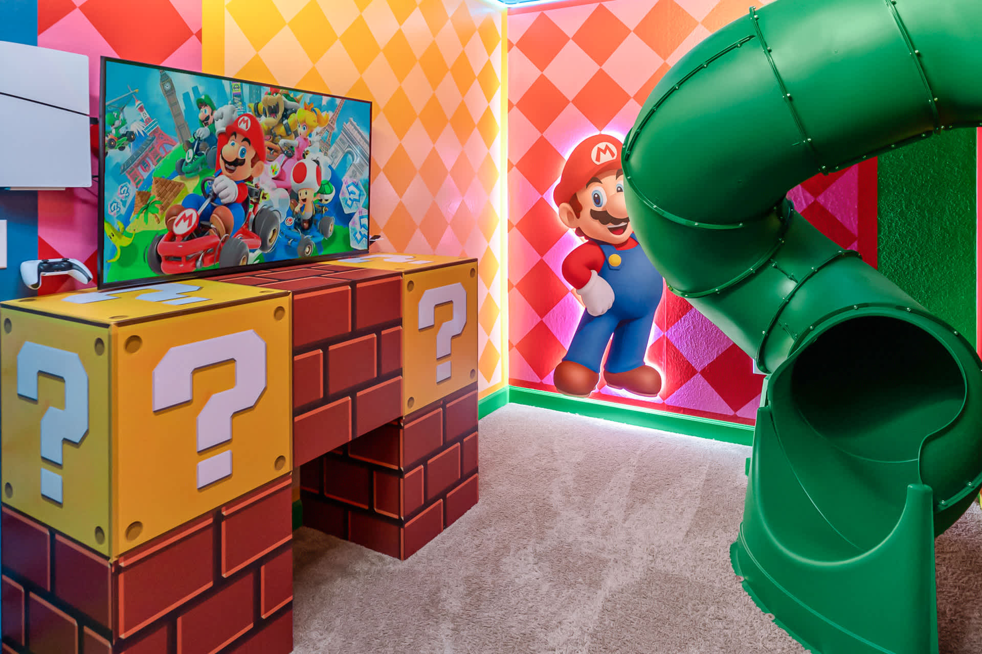 Close-up of the "Super Mario" themed room, highlighting a large TV displaying Mario Kart, set on question block-themed furniture, with a Mario character cutout and colorful checkered walls.