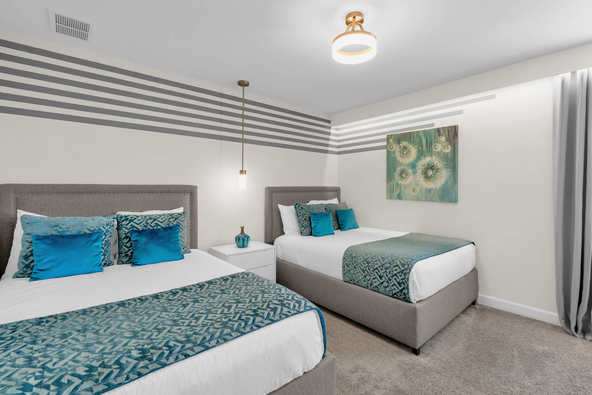 Kids' bedroom featuring two gray upholstered beds, one queen and one full, both with blue accent pillows and teal patterned throws. The walls have horizontal gray and white stripes, and the room includes a modern ceiling light and a pendant light.
