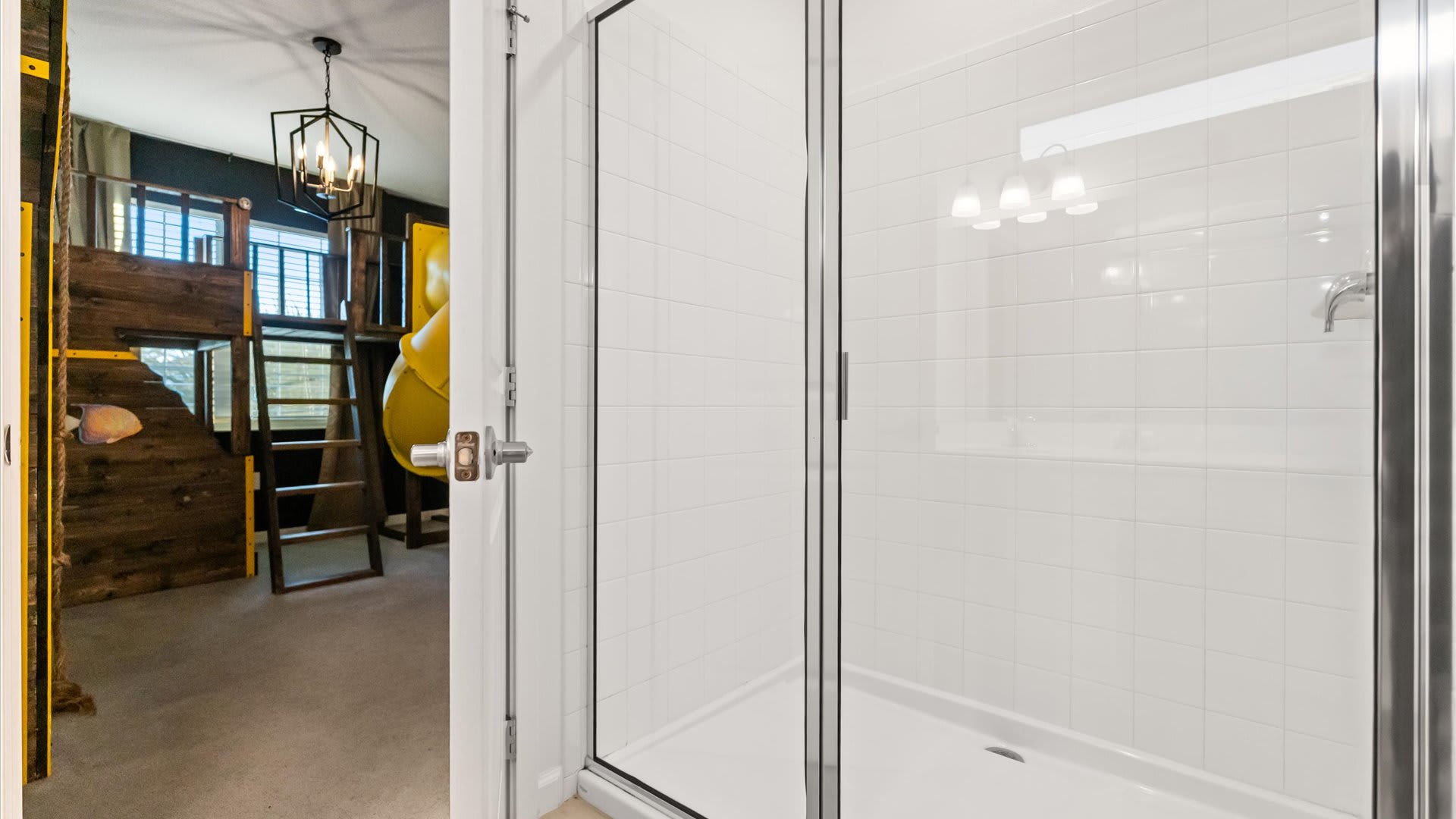 A clear glass shower enclosure with white subway tiles is visible, offering a glimpse into an adjacent themed kids' bedroom with a wooden bunk bed structure and a yellow slide.