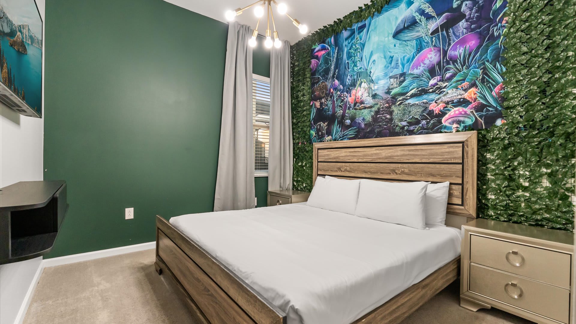 A uniquely themed bedroom with a wooden bed frame and a striking green accent wall adorned with a vibrant, nature-inspired mural featuring mushrooms and foliage. Gold-toned nightstands with lamps flank the bed, and a modern chandelier hangs overhead.