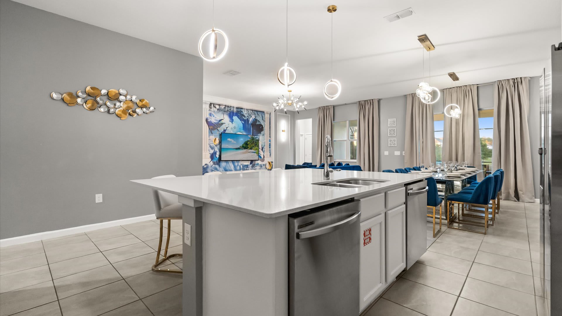 The spacious kitchen island with a white quartz countertop and integrated sink offers bar seating, looking out to the open-concept living and dining areas, with a decorative gold wall art piece on the adjacent wall.