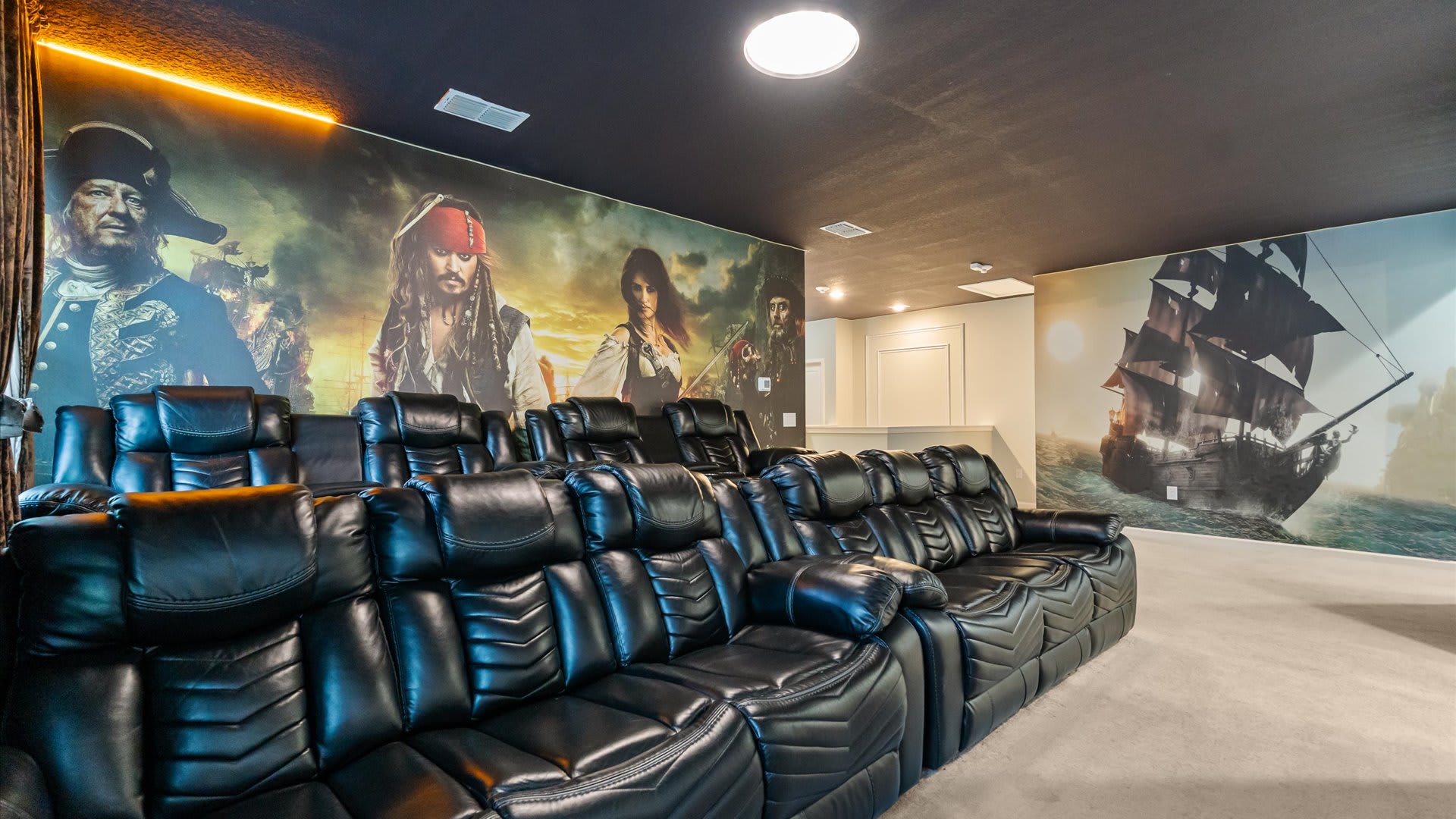 Immersive home cinema with plush black reclining seats arranged in rows, surrounded by a detailed Pirates of the Caribbean mural extending across multiple walls.
