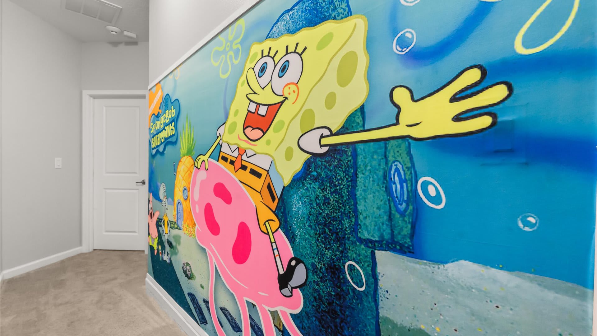 A vibrant, detailed mural depicting Spongebob Squarepants riding a pink jellyfish, with his pineapple house in the background, set against a blue underwater scene.