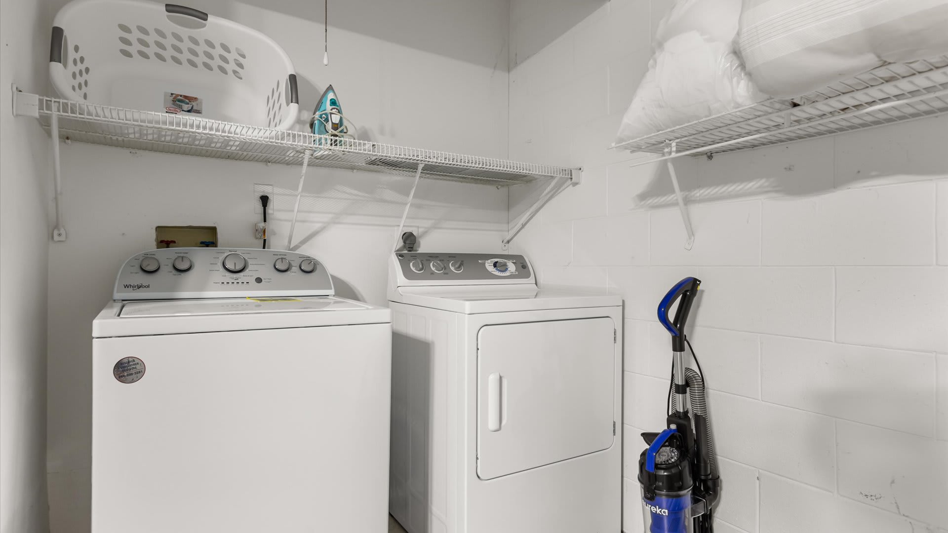 A dedicated laundry room with a white top-loading washing machine and a front-loading dryer. Wire shelving is installed above the appliances and along the wall for storage.
