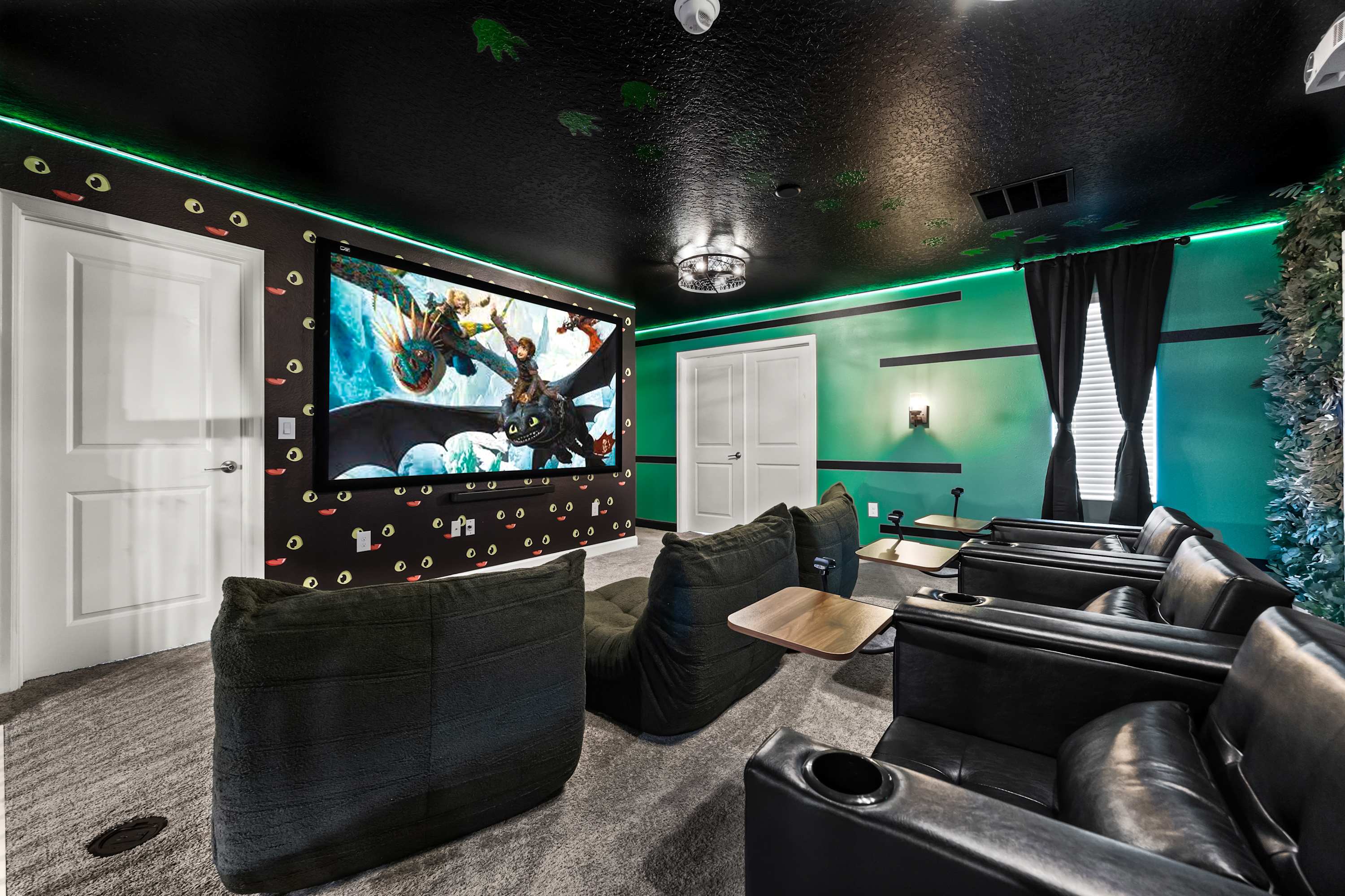 Dark-themed media room with a large projection screen displaying a movie, multiple rows of black recliners and bean bag chairs, and green accent lighting along the walls and ceiling.