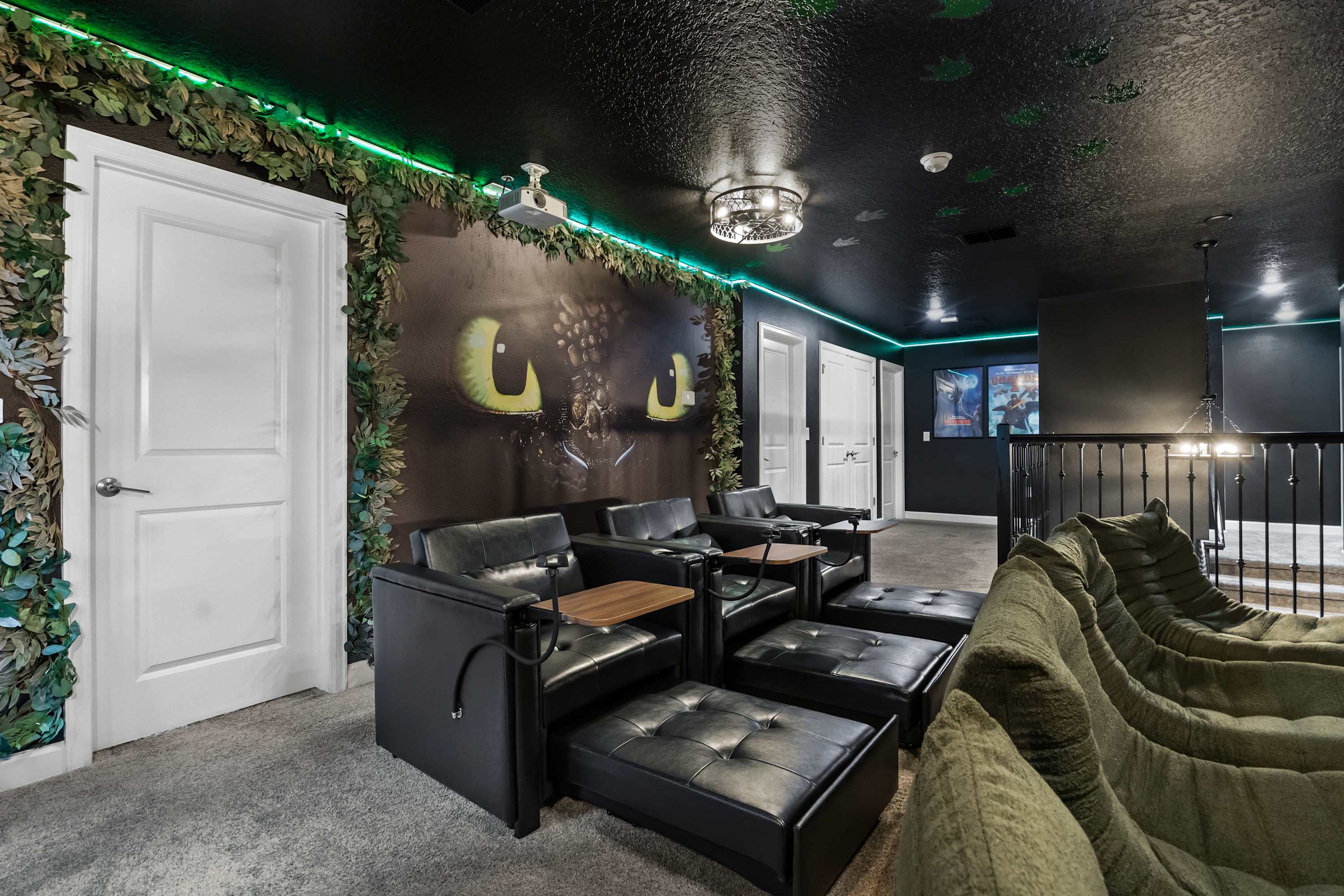 A themed home cinema room featuring a large mural of dragon eyes on the wall, surrounded by green leafy decor and LED strip lighting. Multiple rows of black leather recliners and bean bag chairs provide comfortable seating for movie watching.