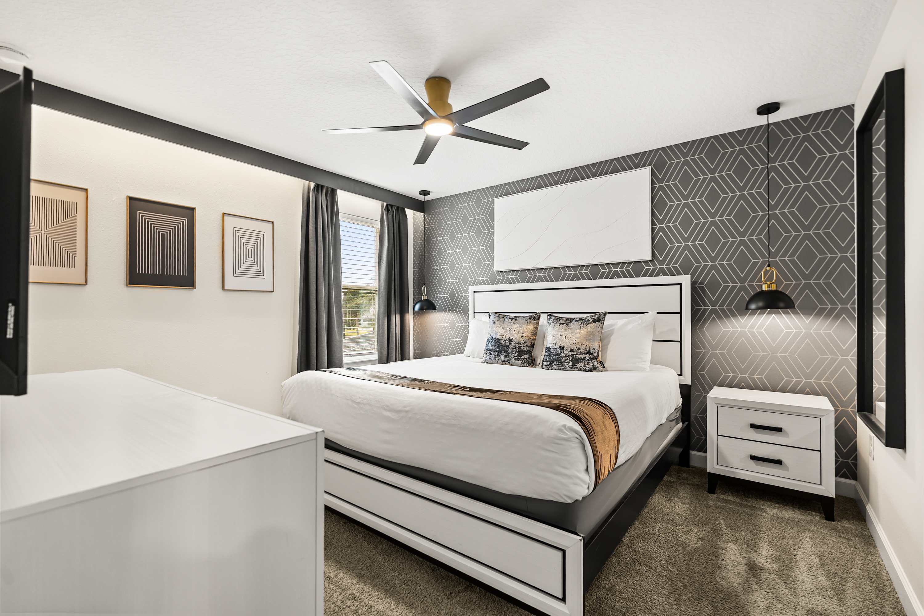 A stylish bedroom featuring a king-sized bed with a white and black frame, geometric gray wallpaper, black pendant lights, and modern abstract wall art, creating a chic and contemporary ambiance.