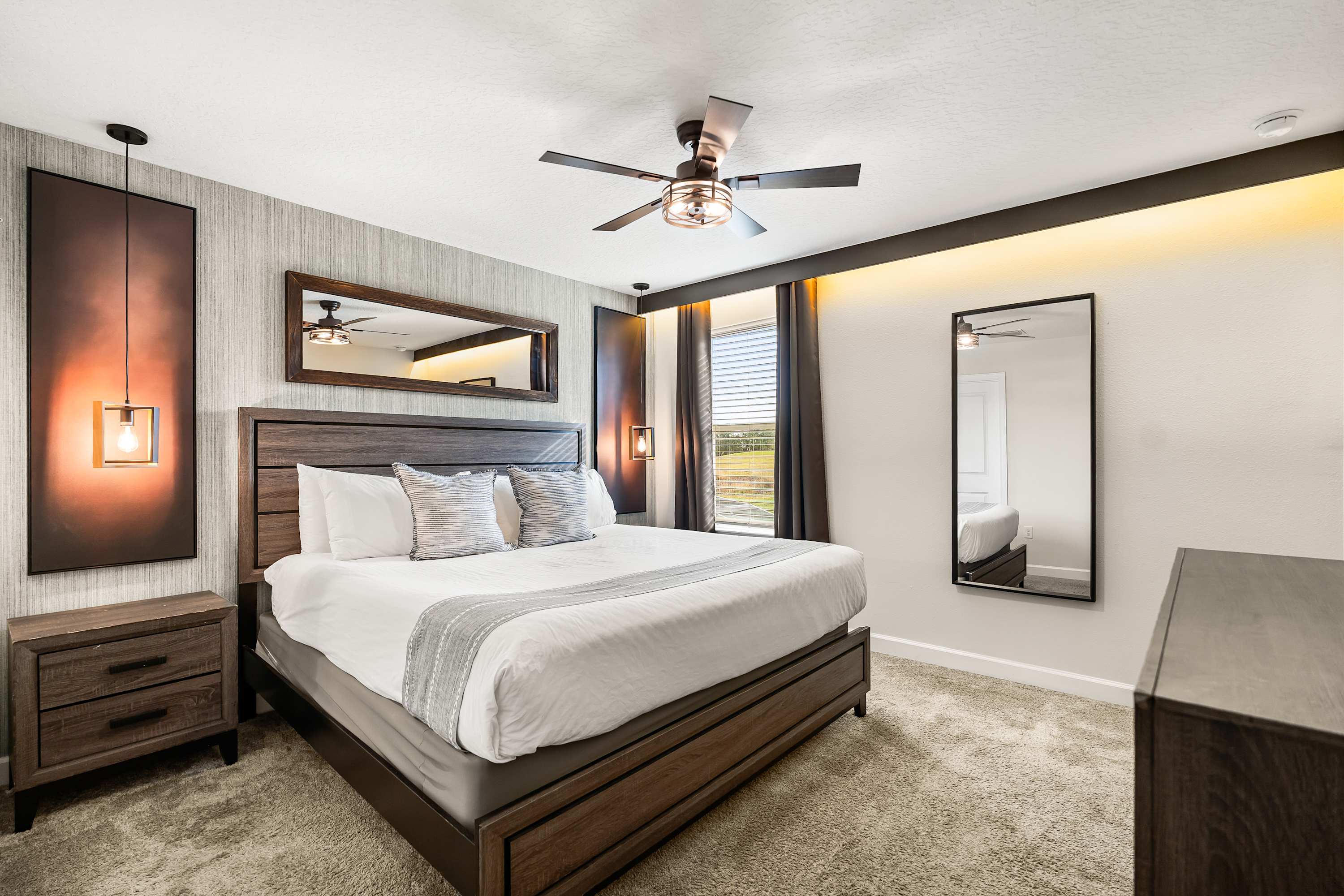 A sophisticated bedroom with a king-sized wooden bed frame and matching nightstands, featuring warm accent lighting, dark wood furniture, and a neutral color palette with a textured accent wall.