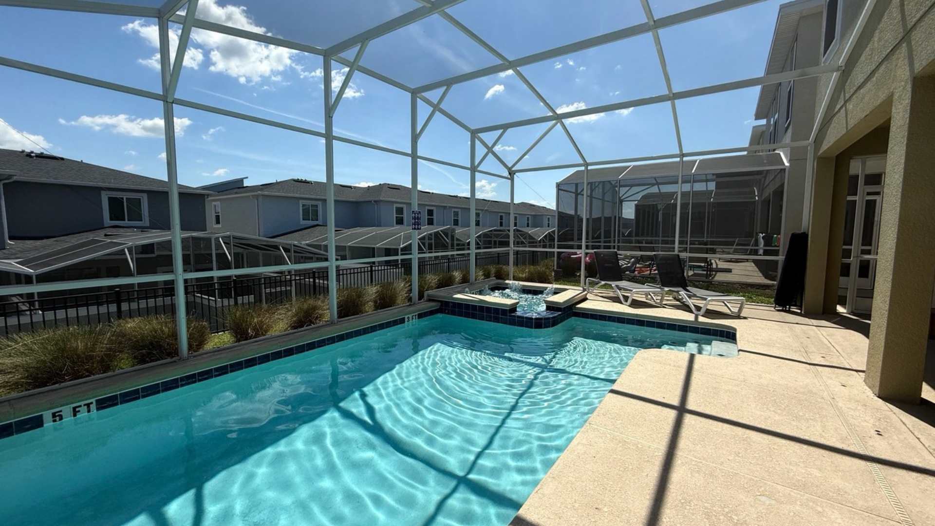 Close-up view of the rectangular swimming pool and integrated hot tub within a large screened enclosure, showing the water features and surrounding concrete deck.