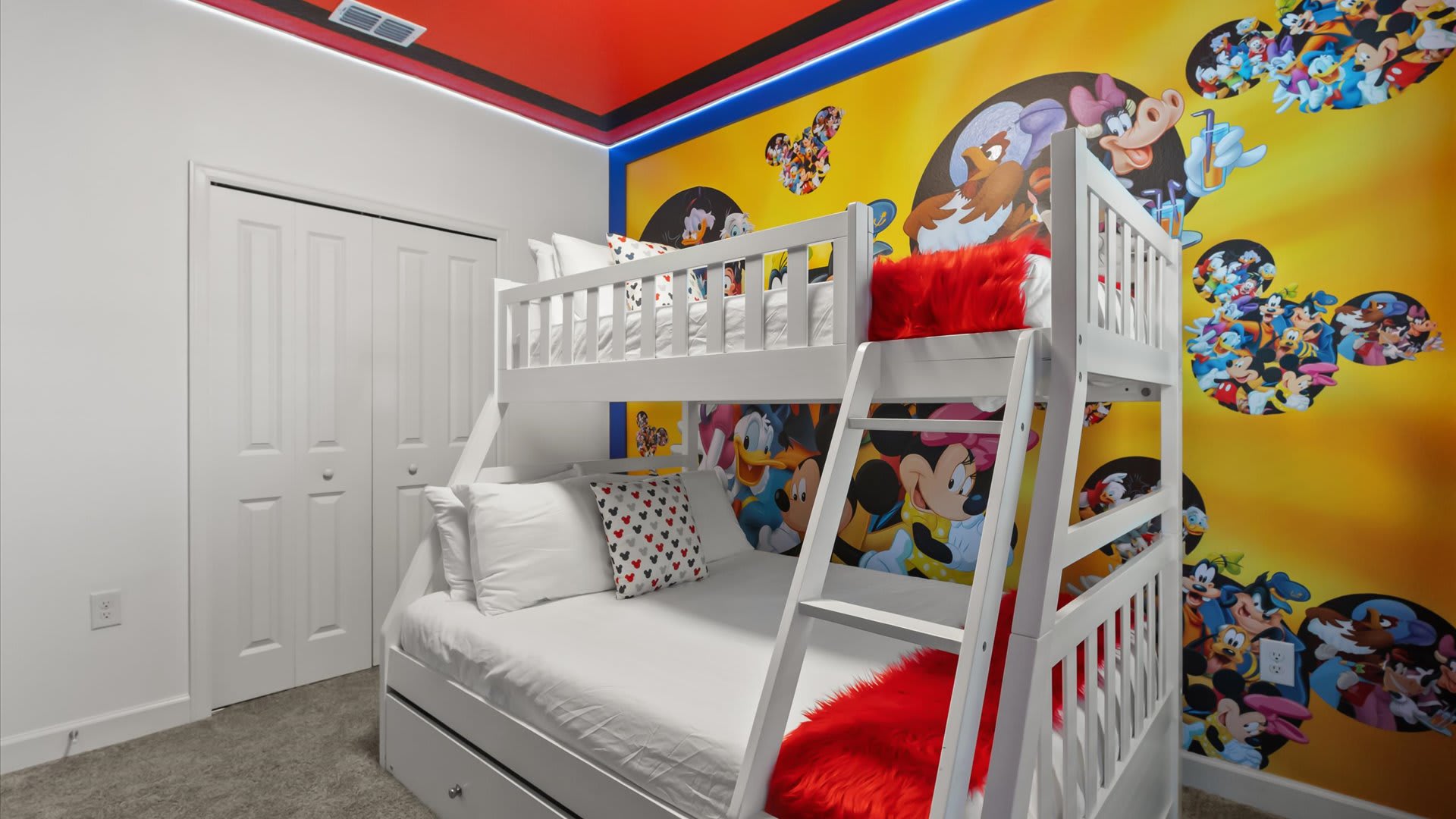 Colorful Disney-themed kids' bedroom with a white bunk bed, bright character wall murals, and a red ceiling. White closet doors are visible on the left.