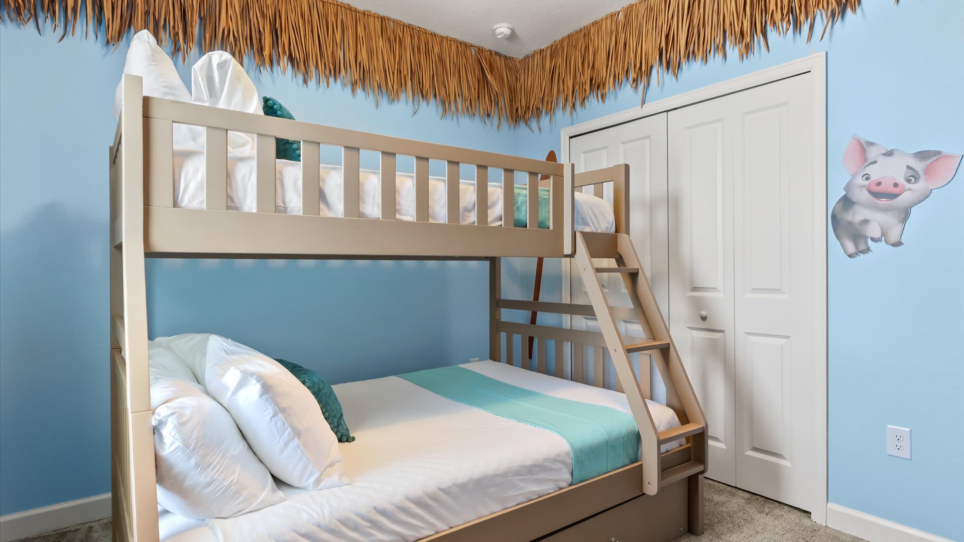 View of the Moana-themed bedroom showcasing a light wood bunk bed with white bedding and teal accents, and a white closet with double doors. A Pua character cutout is visible on the light blue wall.